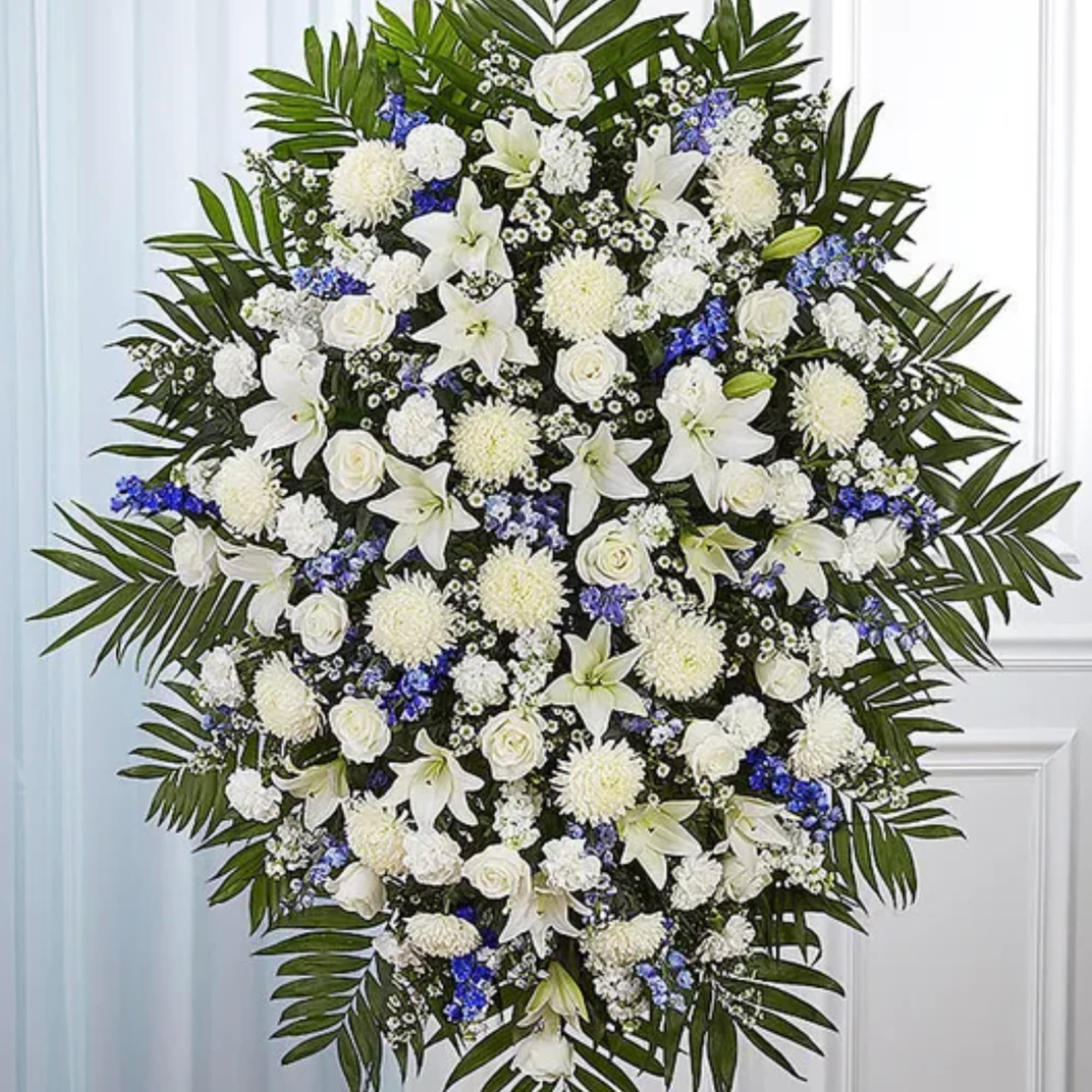 Large white floral standing spray with lilies, roses, and blue accents