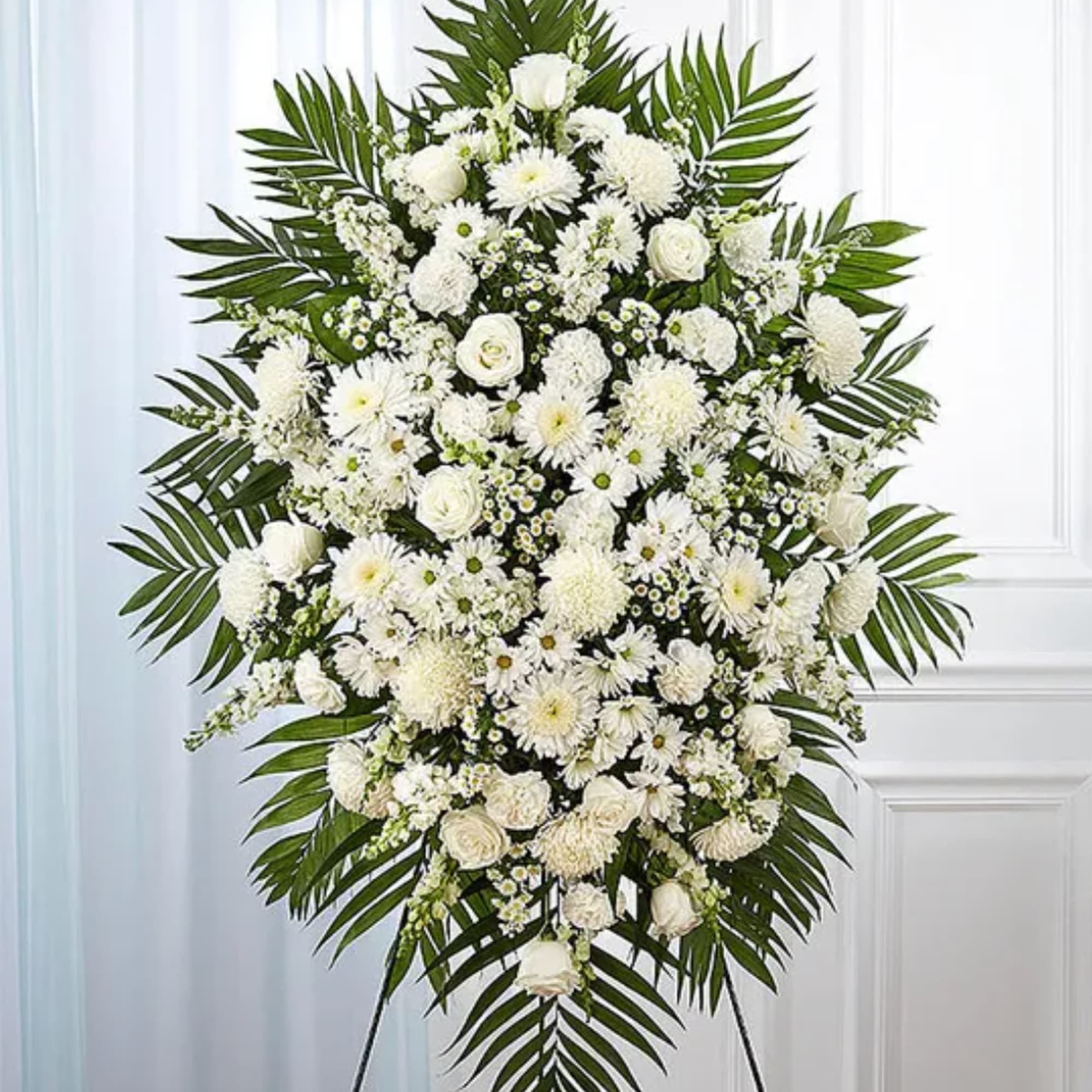 Large white funeral spray with mixed blooms and palm fronds on an easel