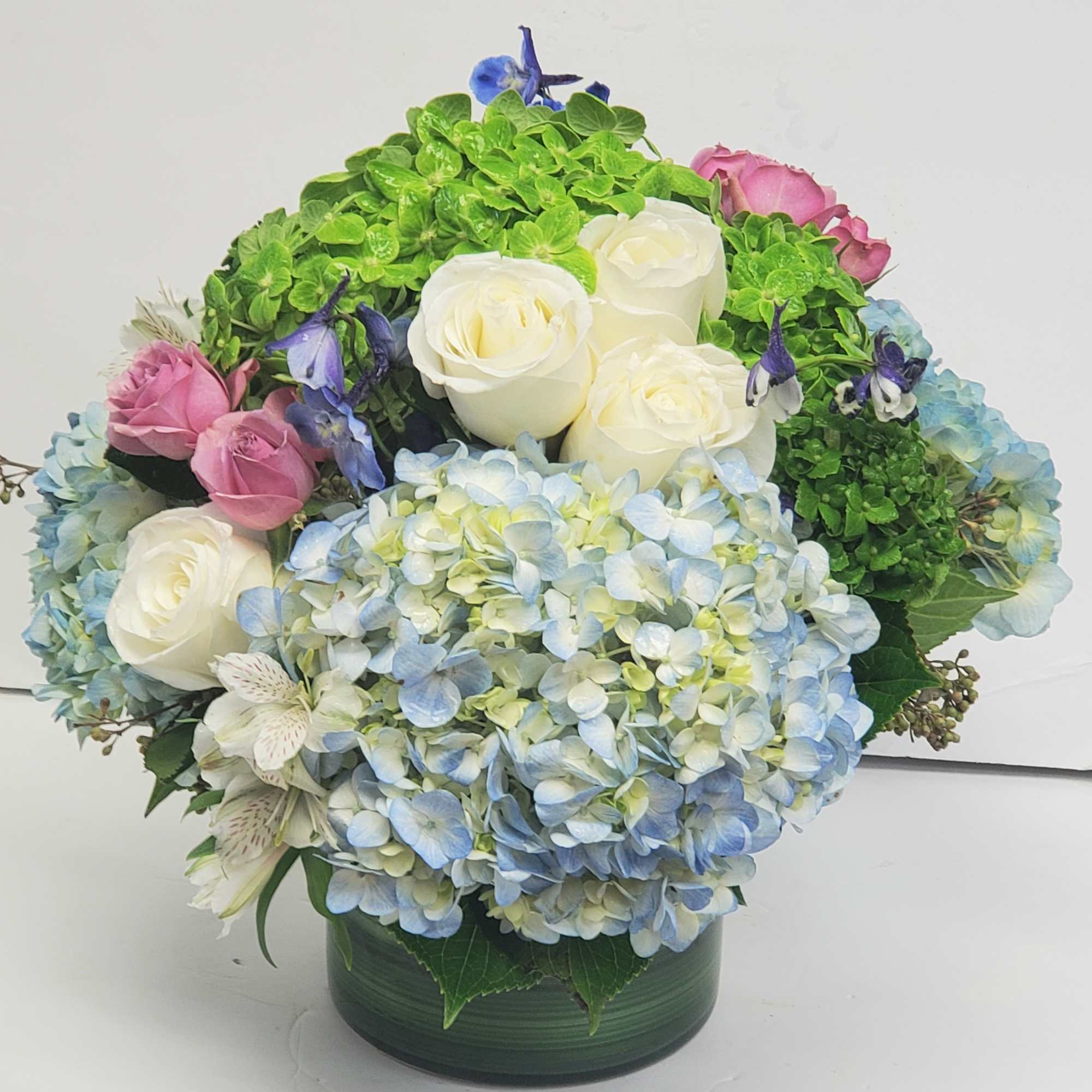 Bouquet of white roses, blue hydrangeas, and pink roses in a green vase
