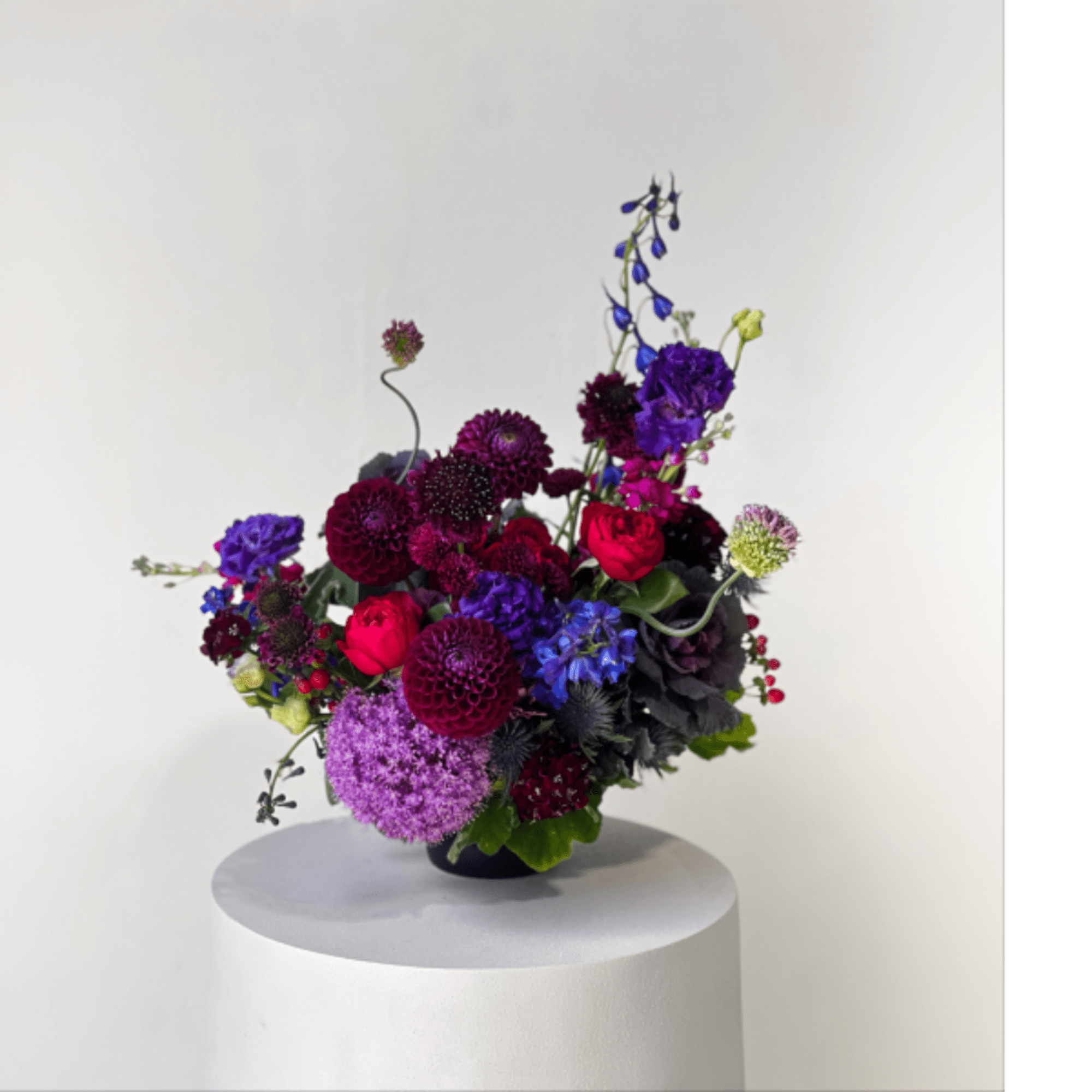 Colorful mixed bouquet in a low dark vase on a white pedestal