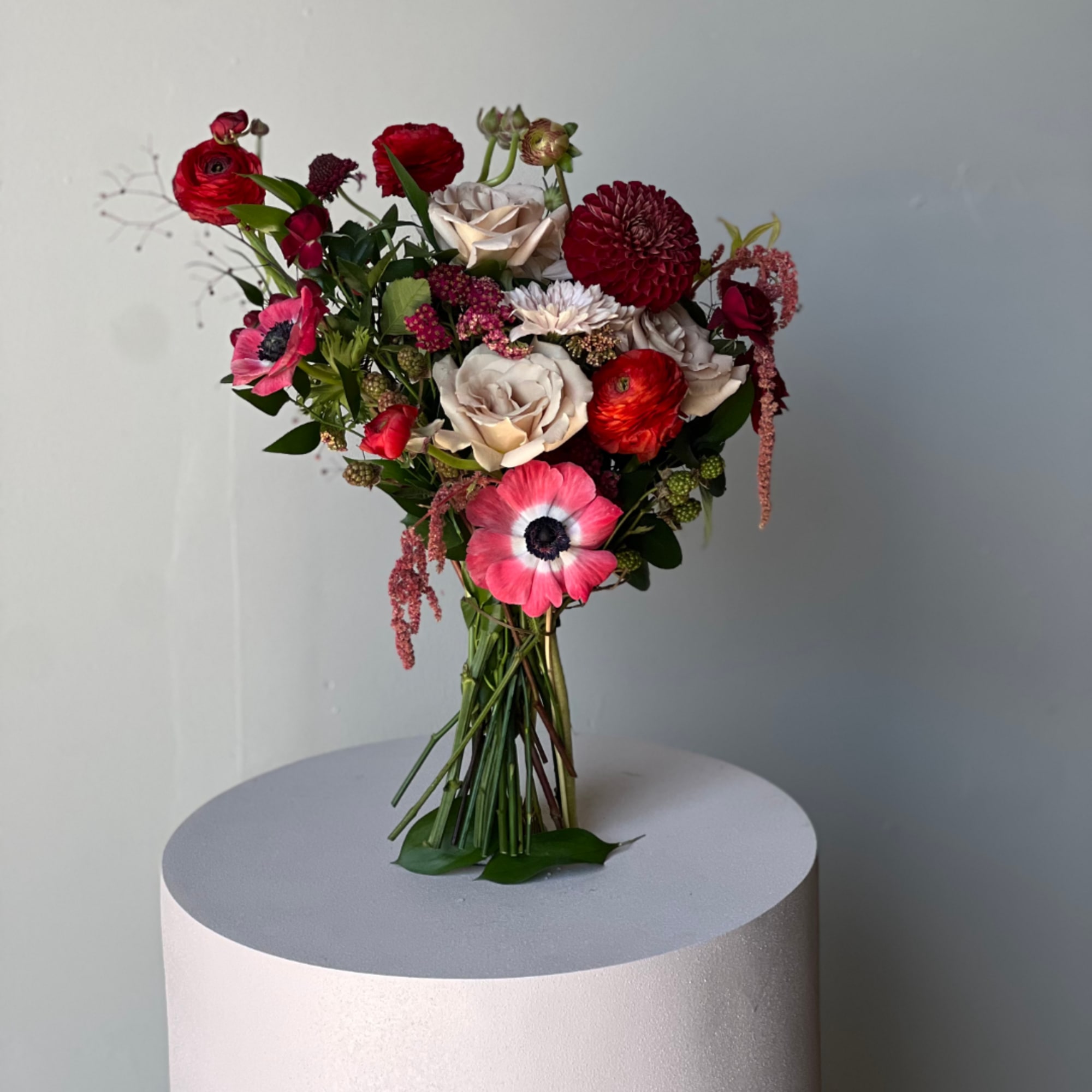 Hand-tied bouquet of red, blush, and pink flowers on a pedestal