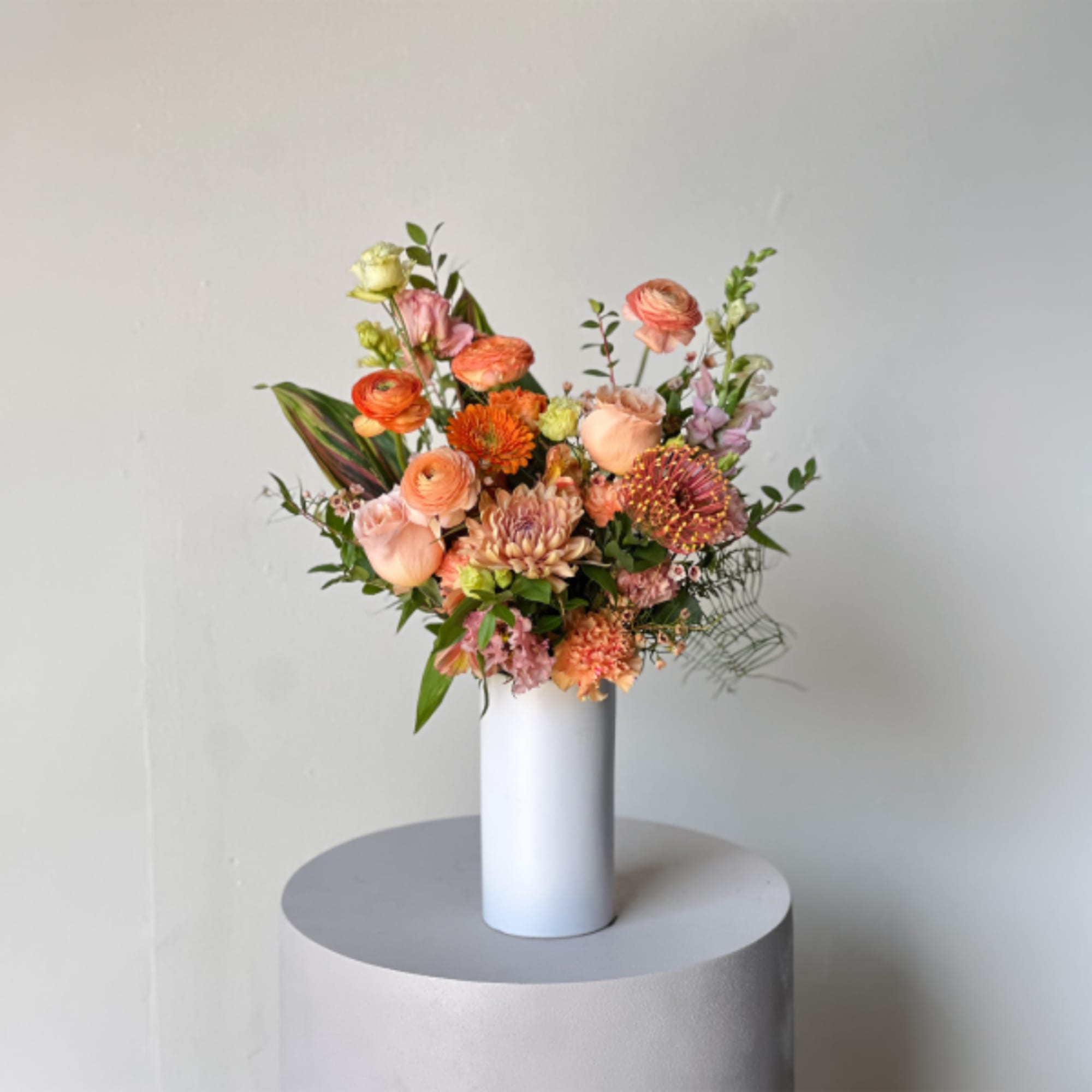 Mixed peach and pink flowers in a tall white vase