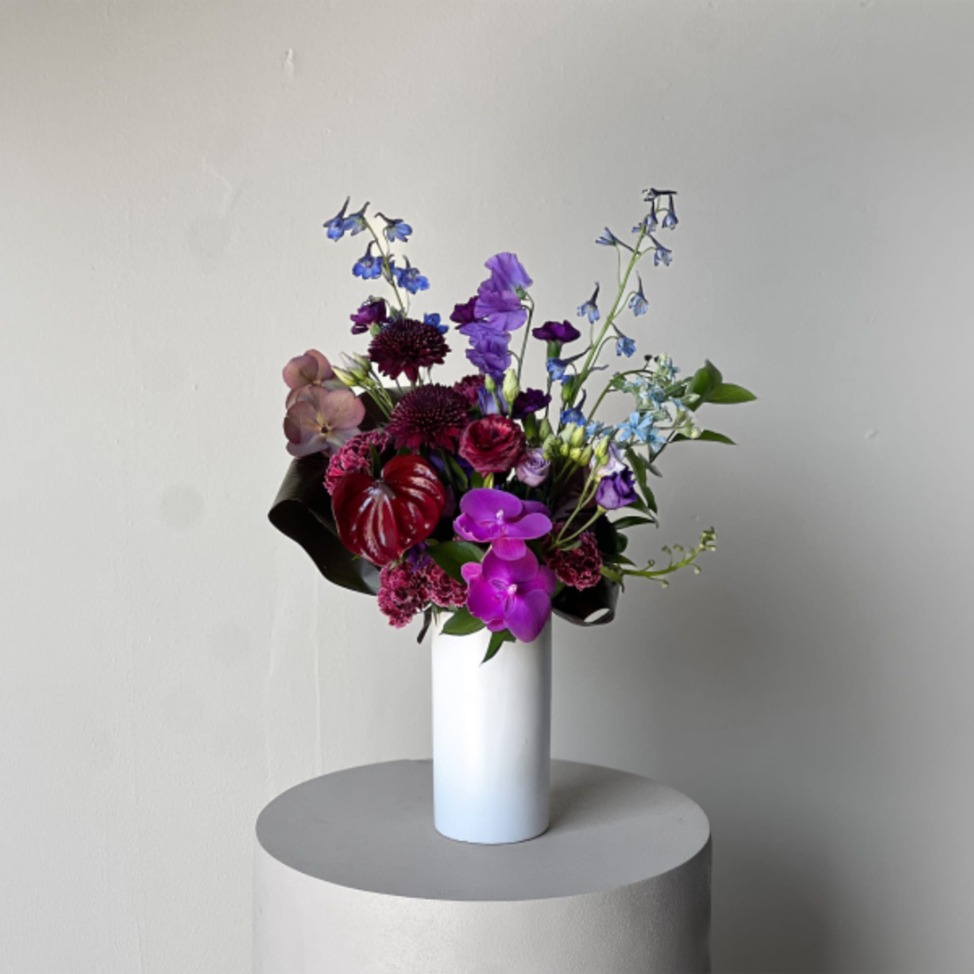 Purple and blue mixed bouquet in a white cylindrical vase