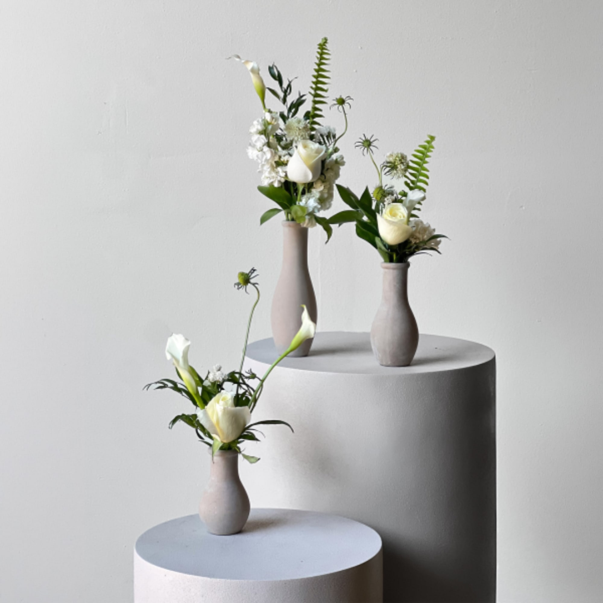 Three small white floral arrangements in matte vases on pedestals