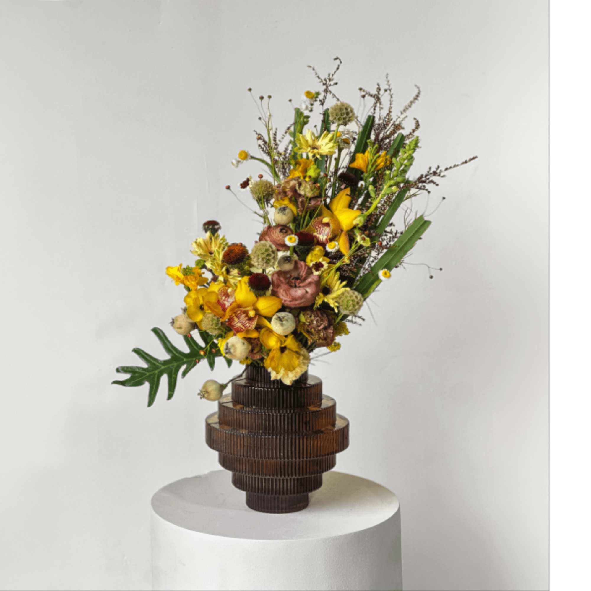Tall floral arrangement with yellow blooms in a brown sculptural vase