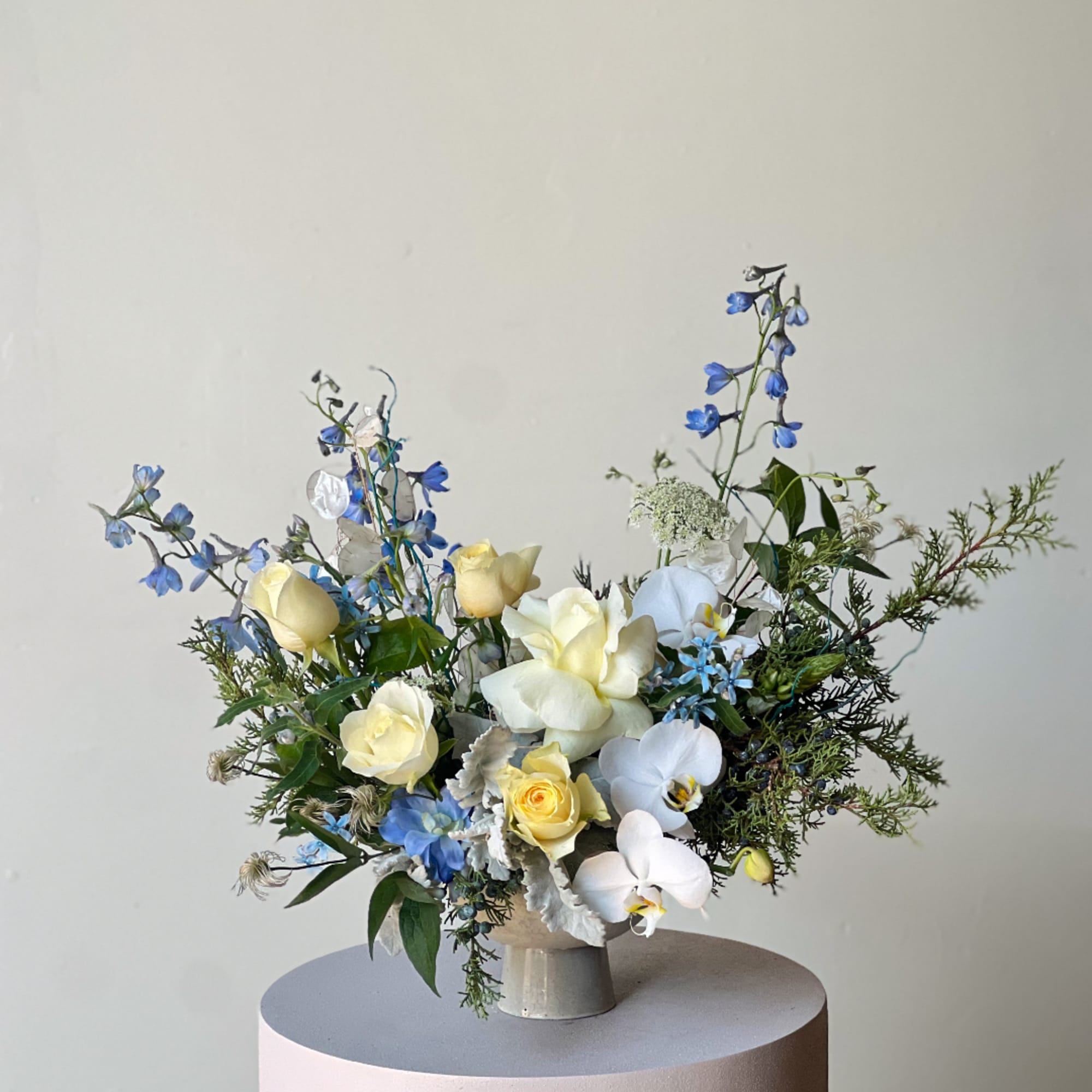 Blue and white floral arrangement with pale yellow roses in a ceramic vase
