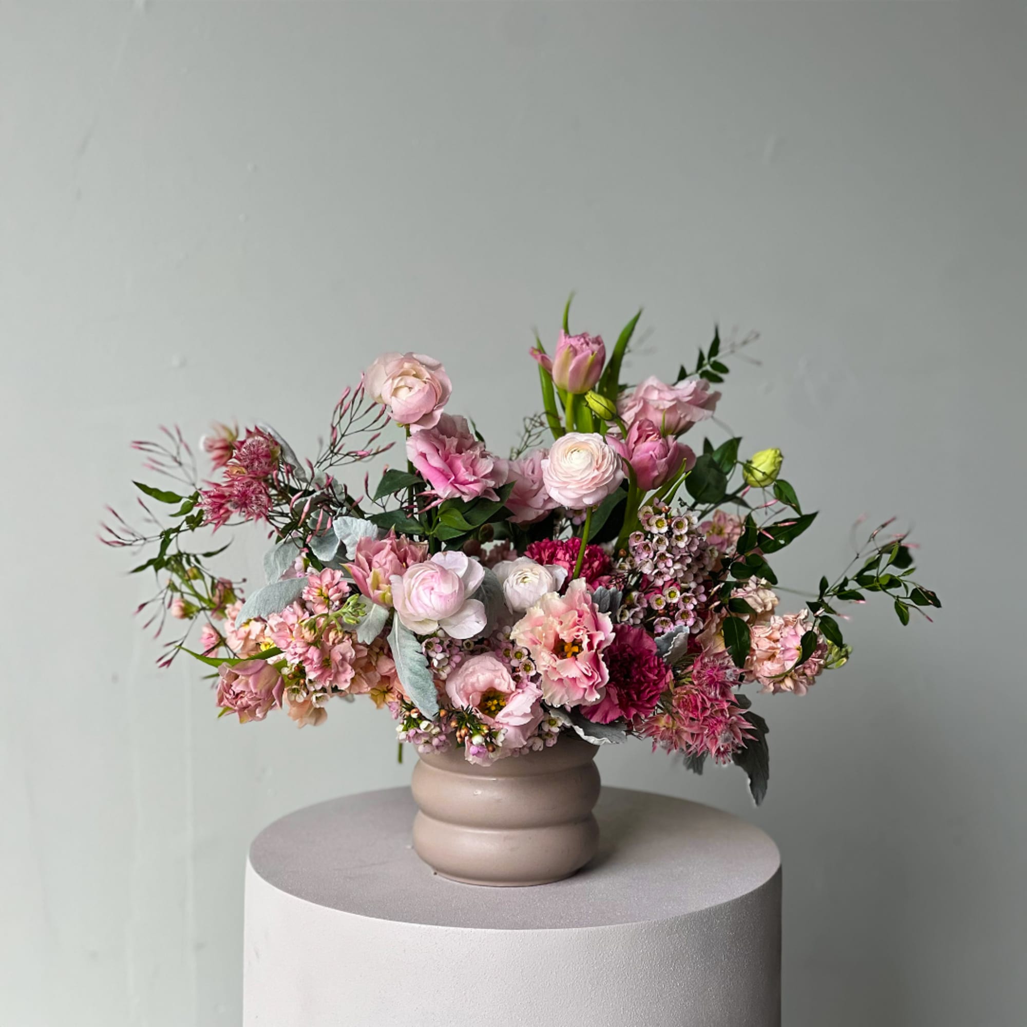 Pink mixed flower arrangement in a beige vase