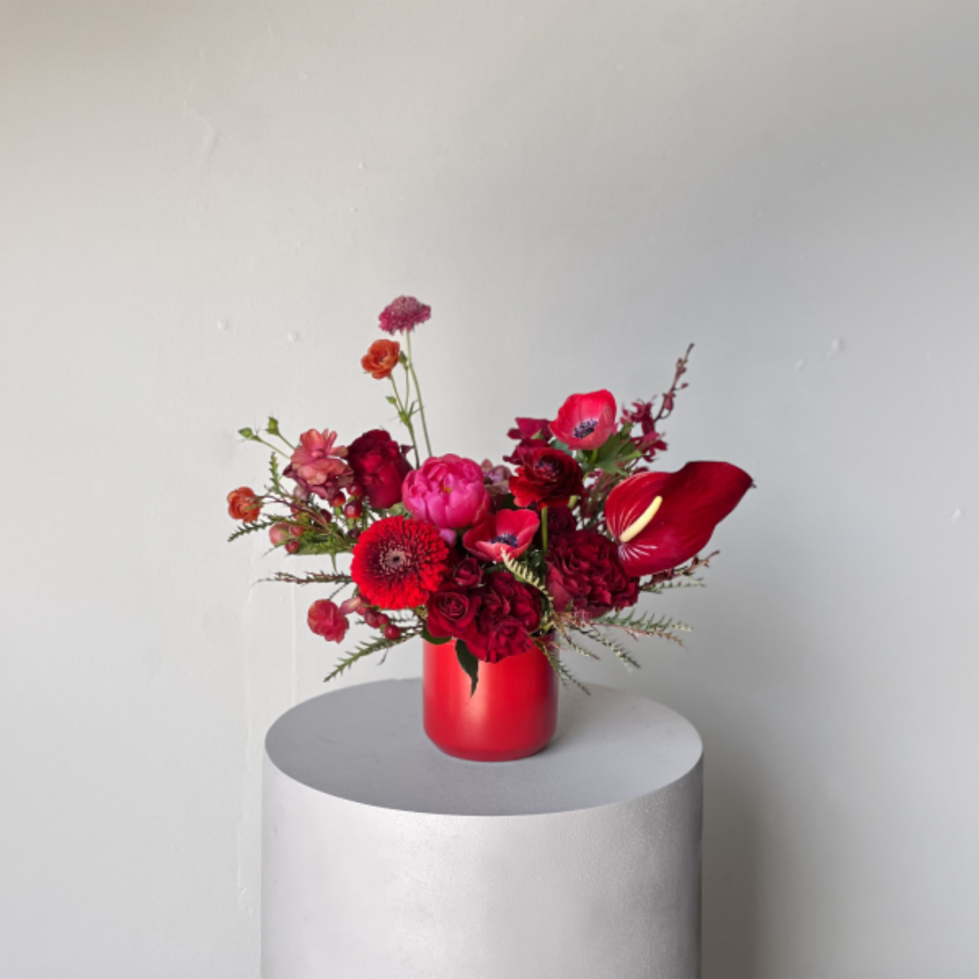 Red floral arrangement in a red vase on a pedestal