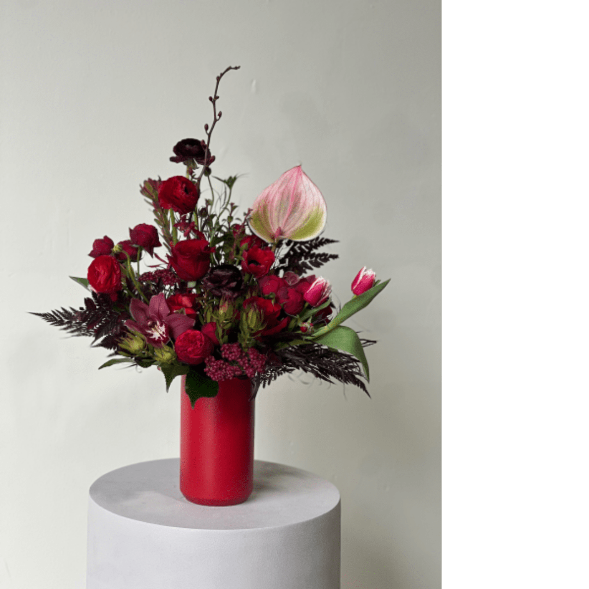 Red and pink floral arrangement in a tall red vase