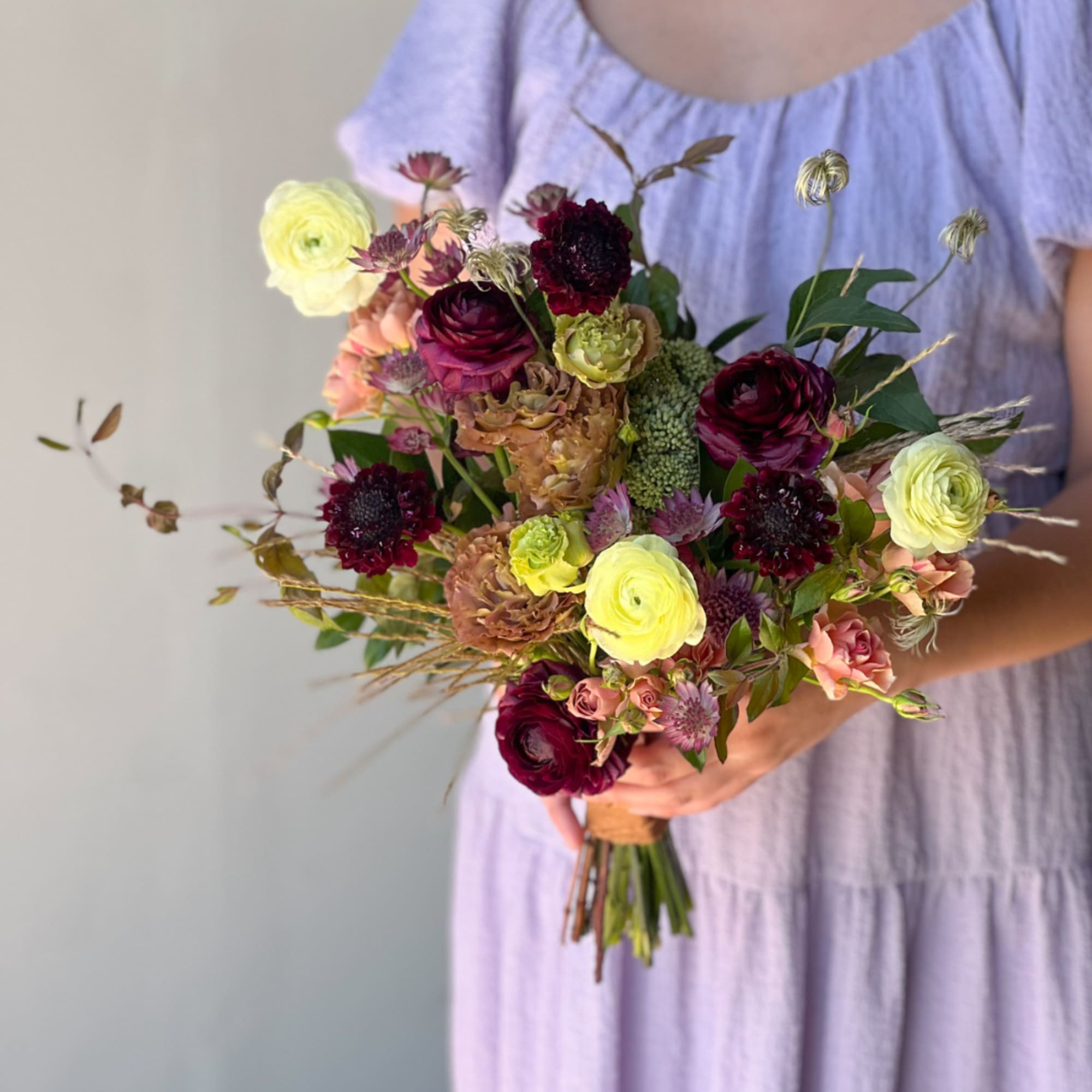 Handheld bouquet of burgundy, yellow, and pink flowers