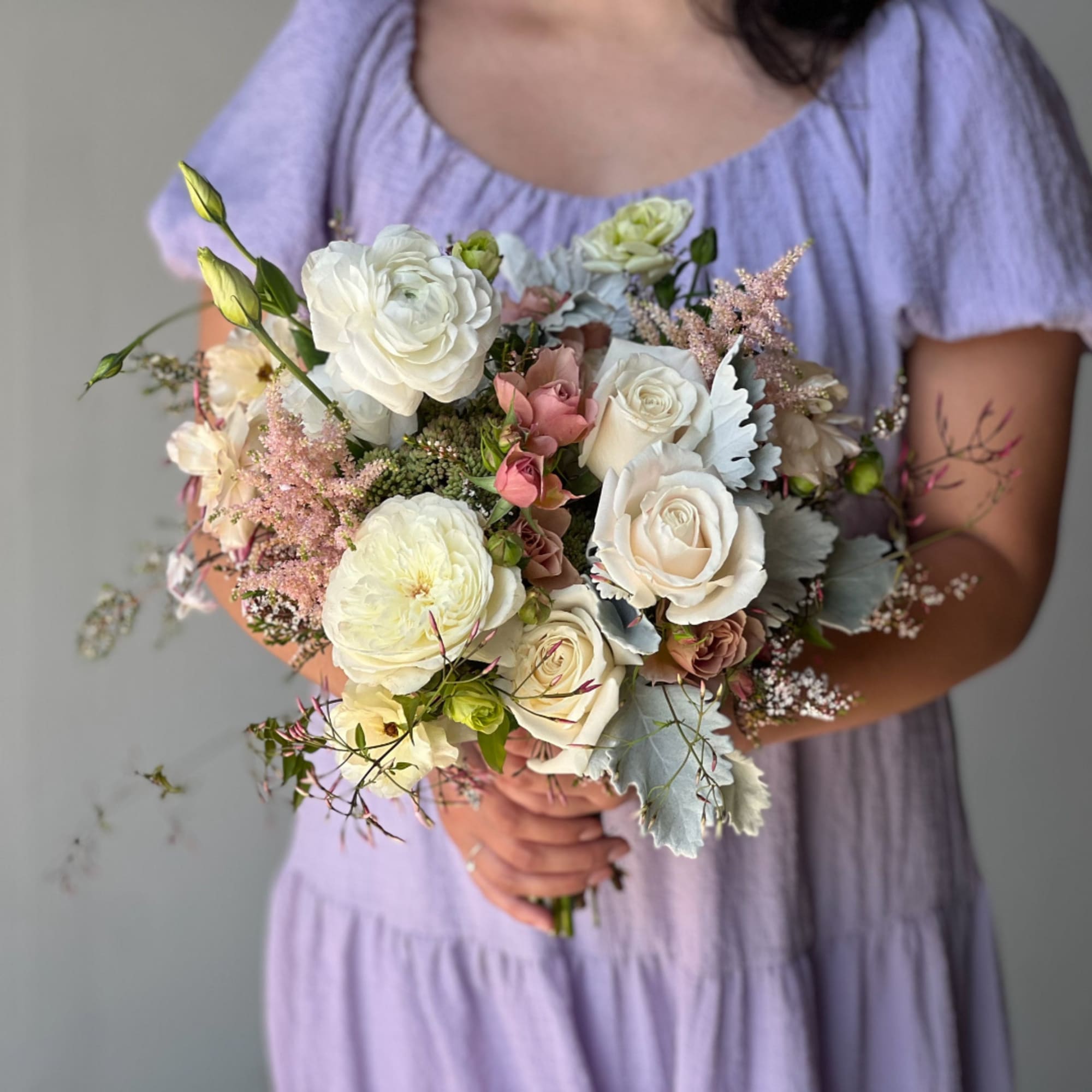 Person holding a bouquet of white and blush roses with pale filler flowers