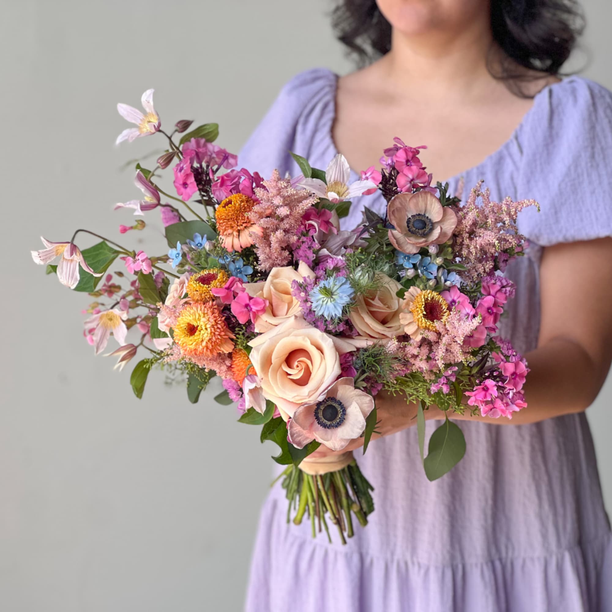 Woman holding a pastel bouquet of roses, anemones, and mixed blooms