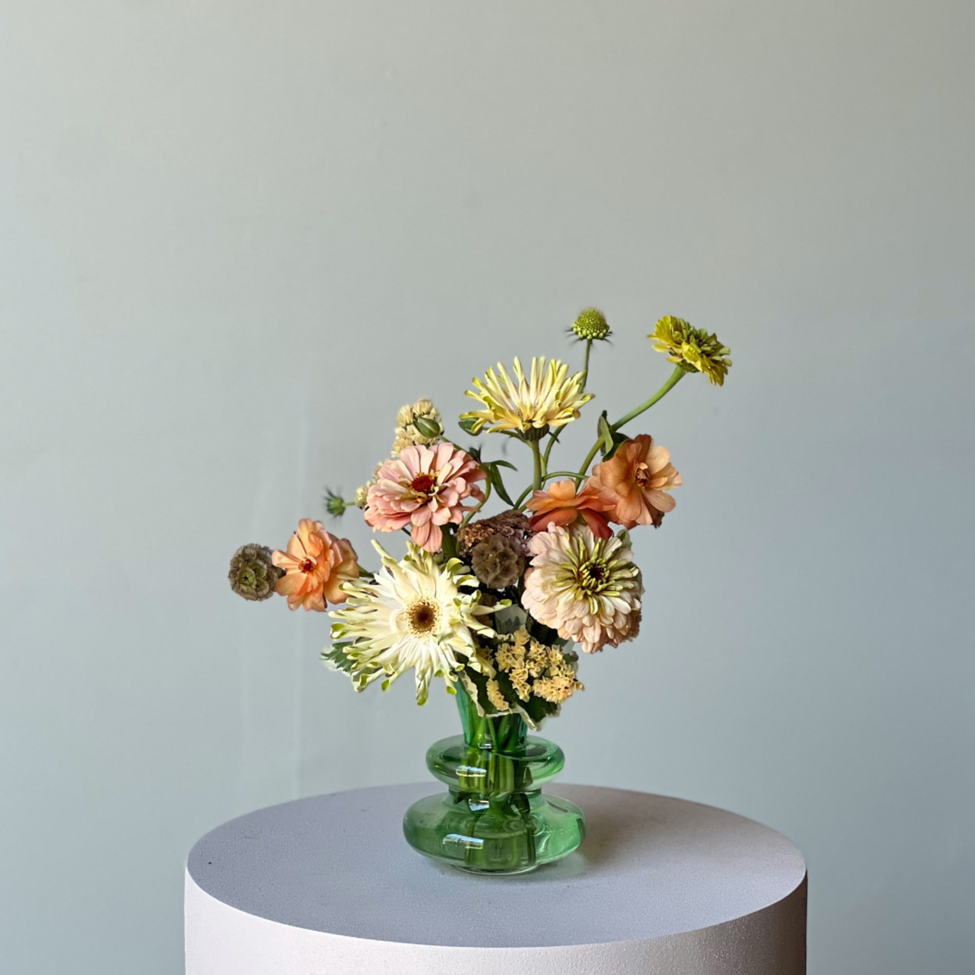 Mixed pastel flowers in a green glass vase on a round pedestal