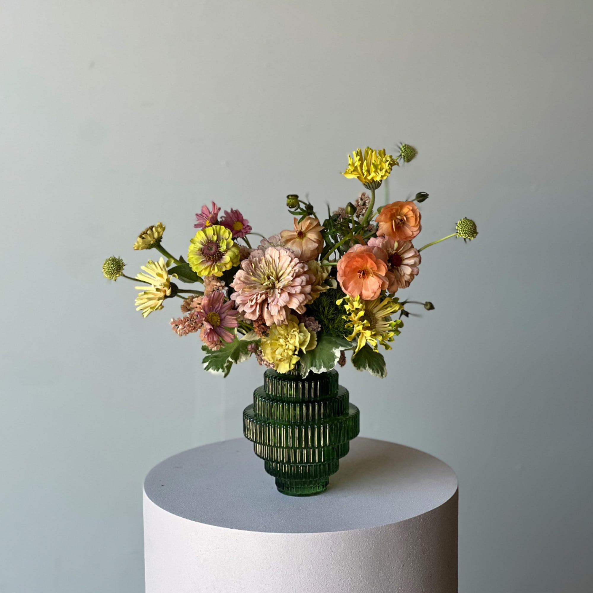 Mixed pastel flowers in a dark green ribbed vase on a pedestal