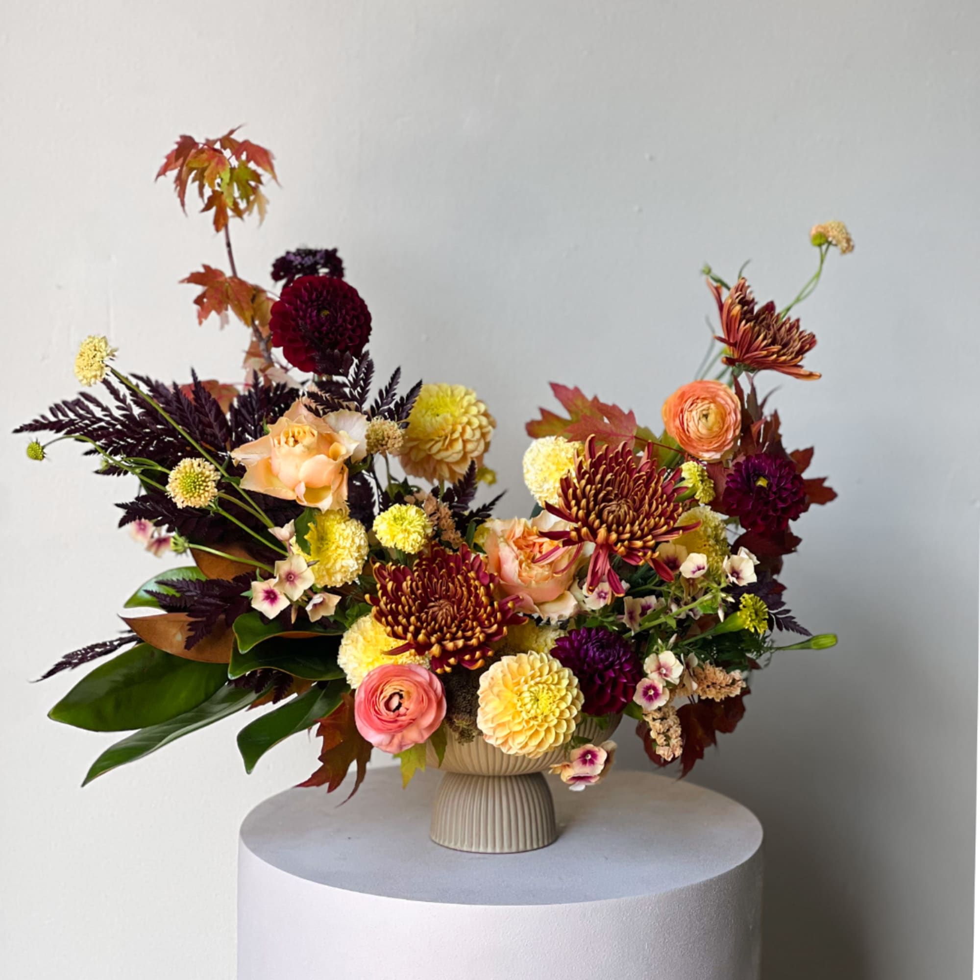 Mixed floral arrangement in a cream vase with burgundy, peach, and yellow blooms