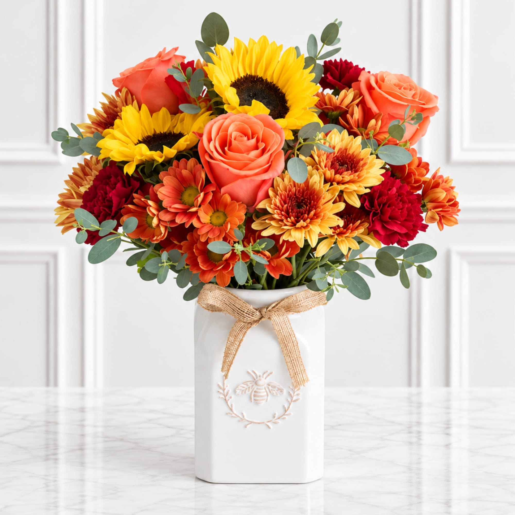 Bouquet of sunflowers, roses, and mums in a white vase with a ribbon