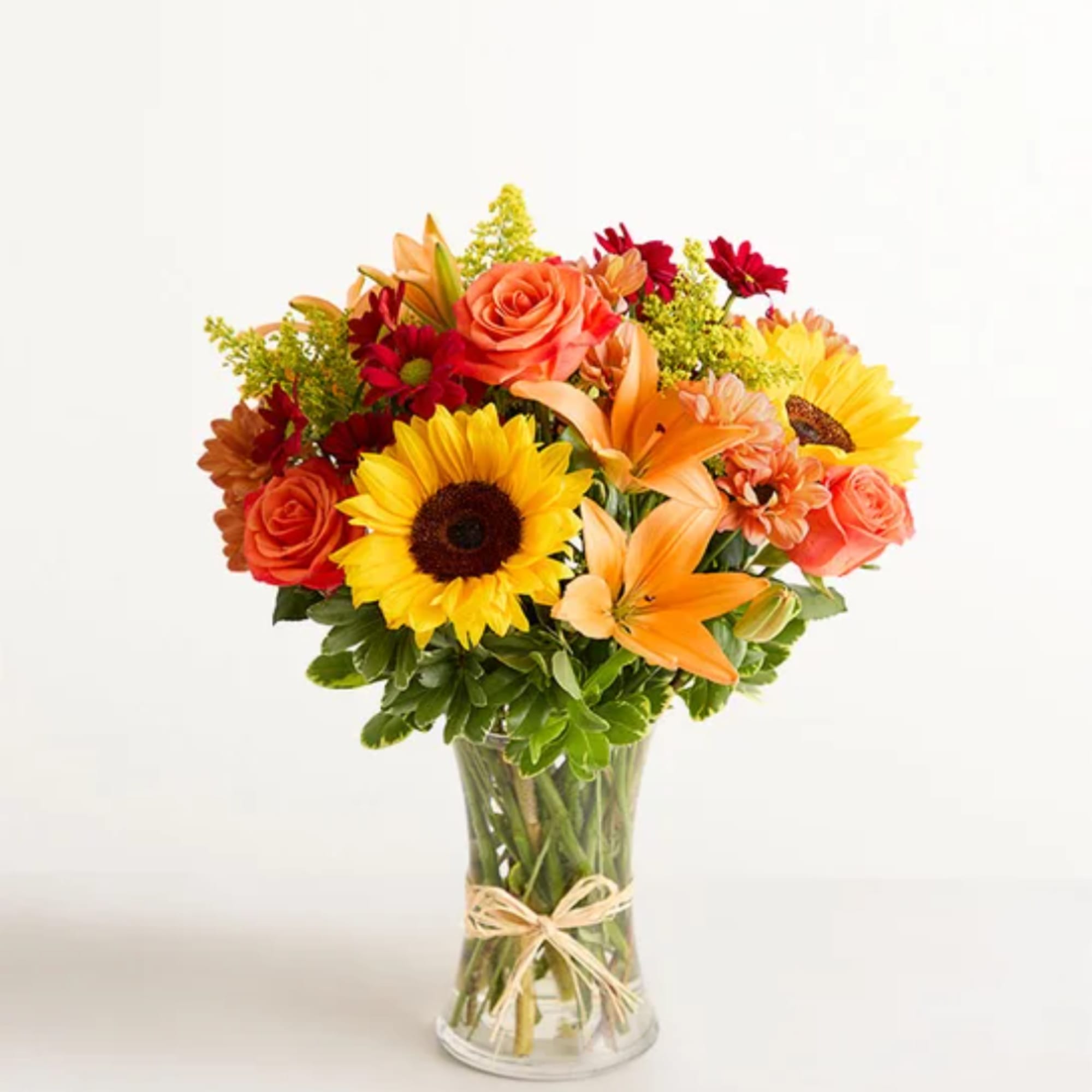 Bouquet of sunflowers, roses, and lilies in a clear glass vase