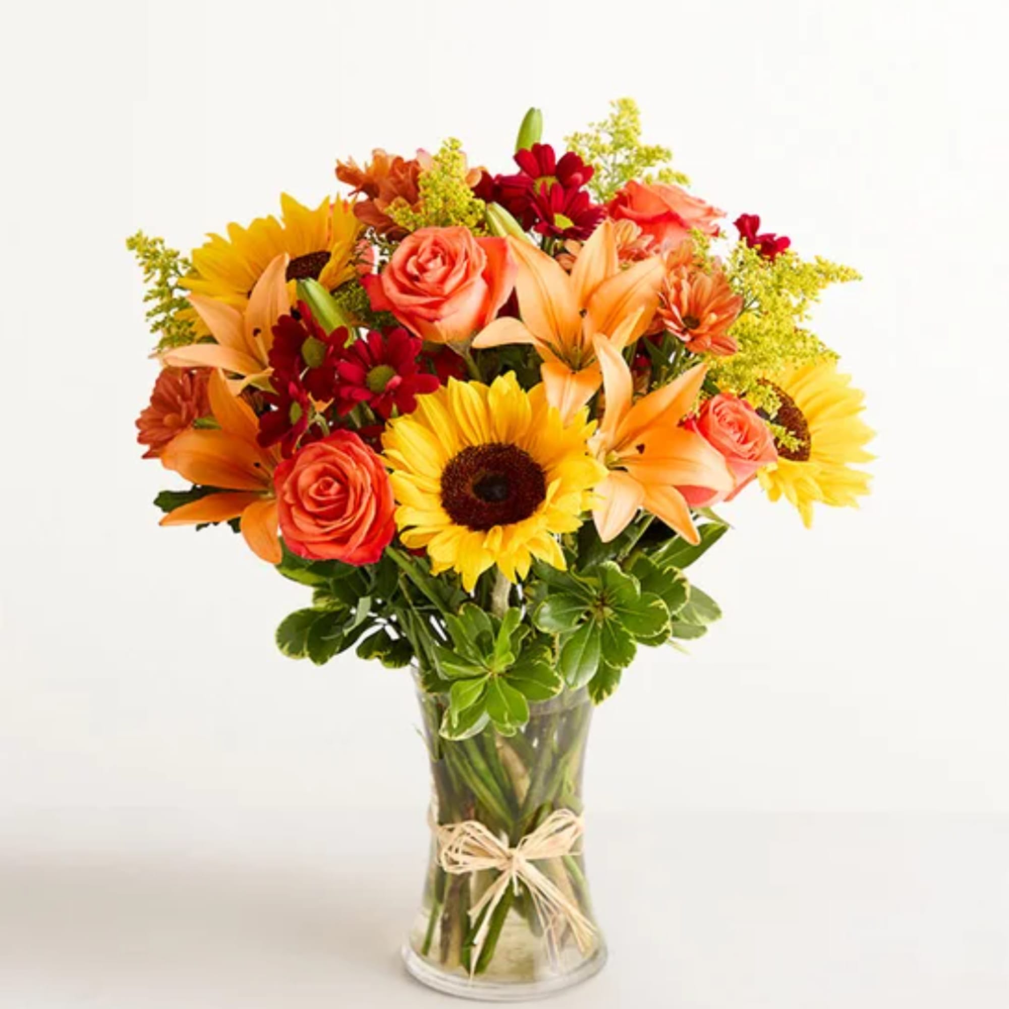 Mixed bouquet of sunflowers, roses, lilies, and daisies in a glass vase