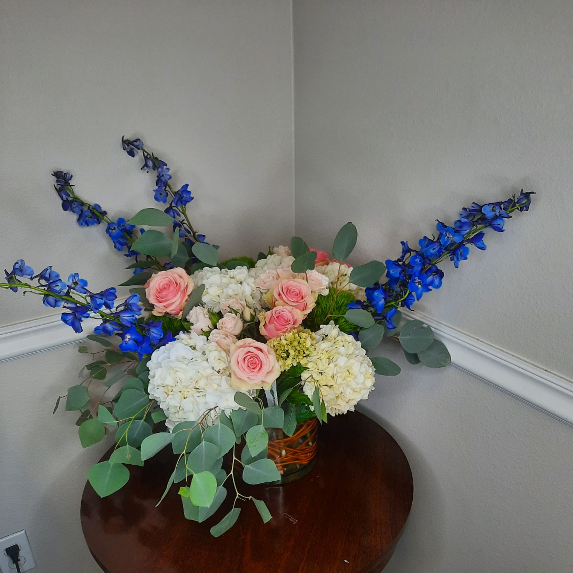 Pink roses and white hydrangeas in a glass vase with blue flowers arching outward