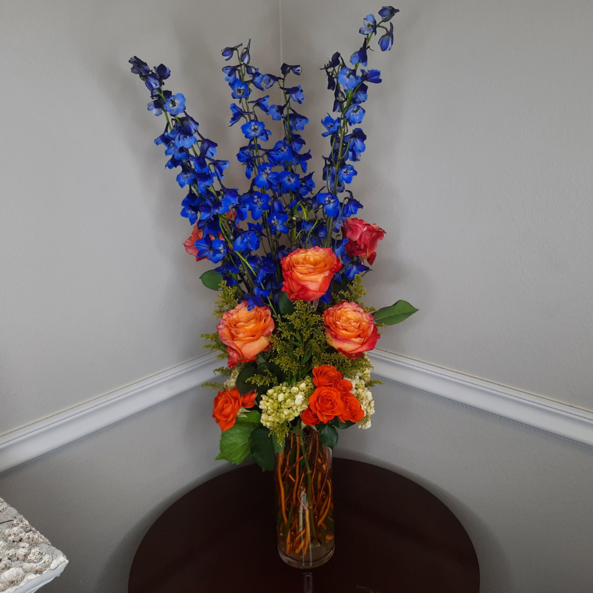 Tall bouquet of blue delphinium and orange roses in a glass vase, photo 2 of 7