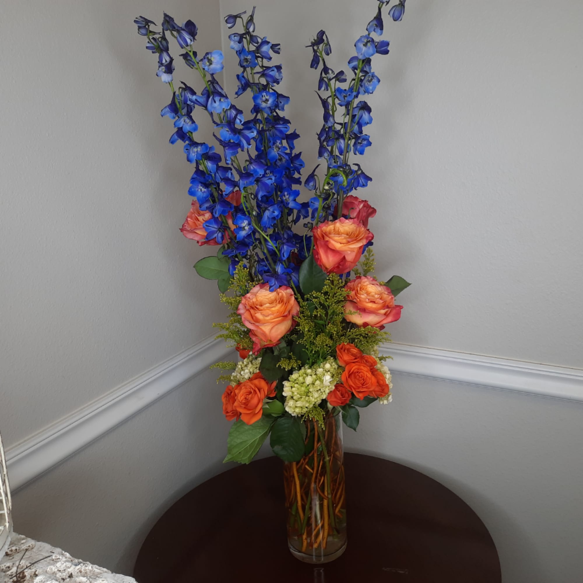 Tall bouquet of blue delphinium and orange roses in a glass vase, photo 3 of 7