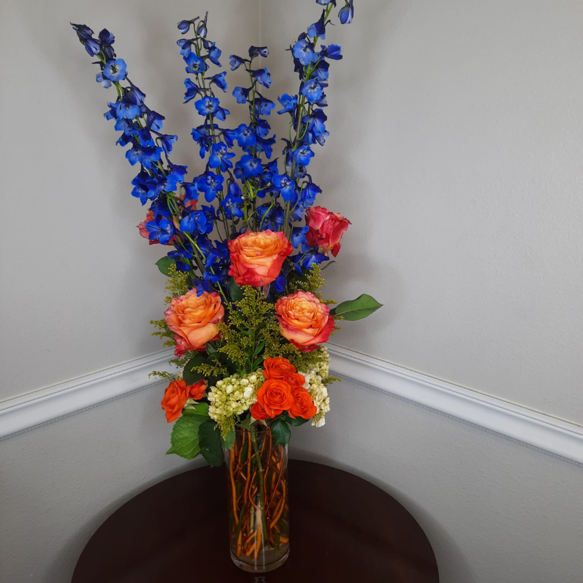 Tall bouquet of blue flowers and orange roses in a glass vase, photo 4 of 7