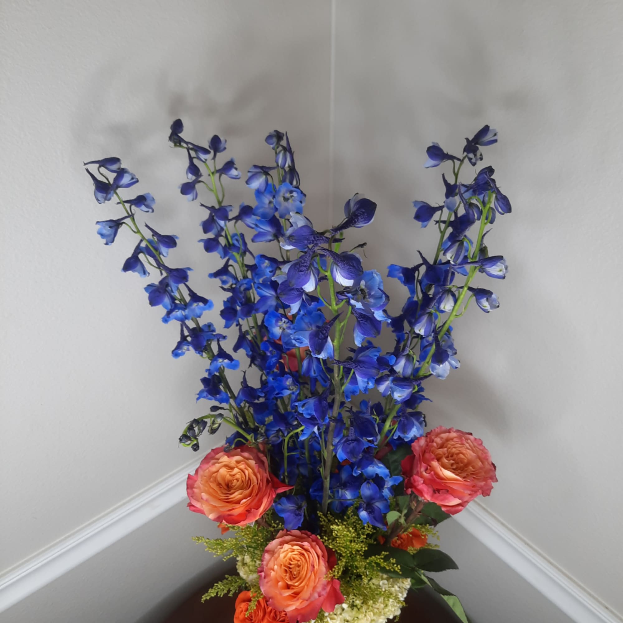 Blue delphinium arrangement with orange roses in a vase