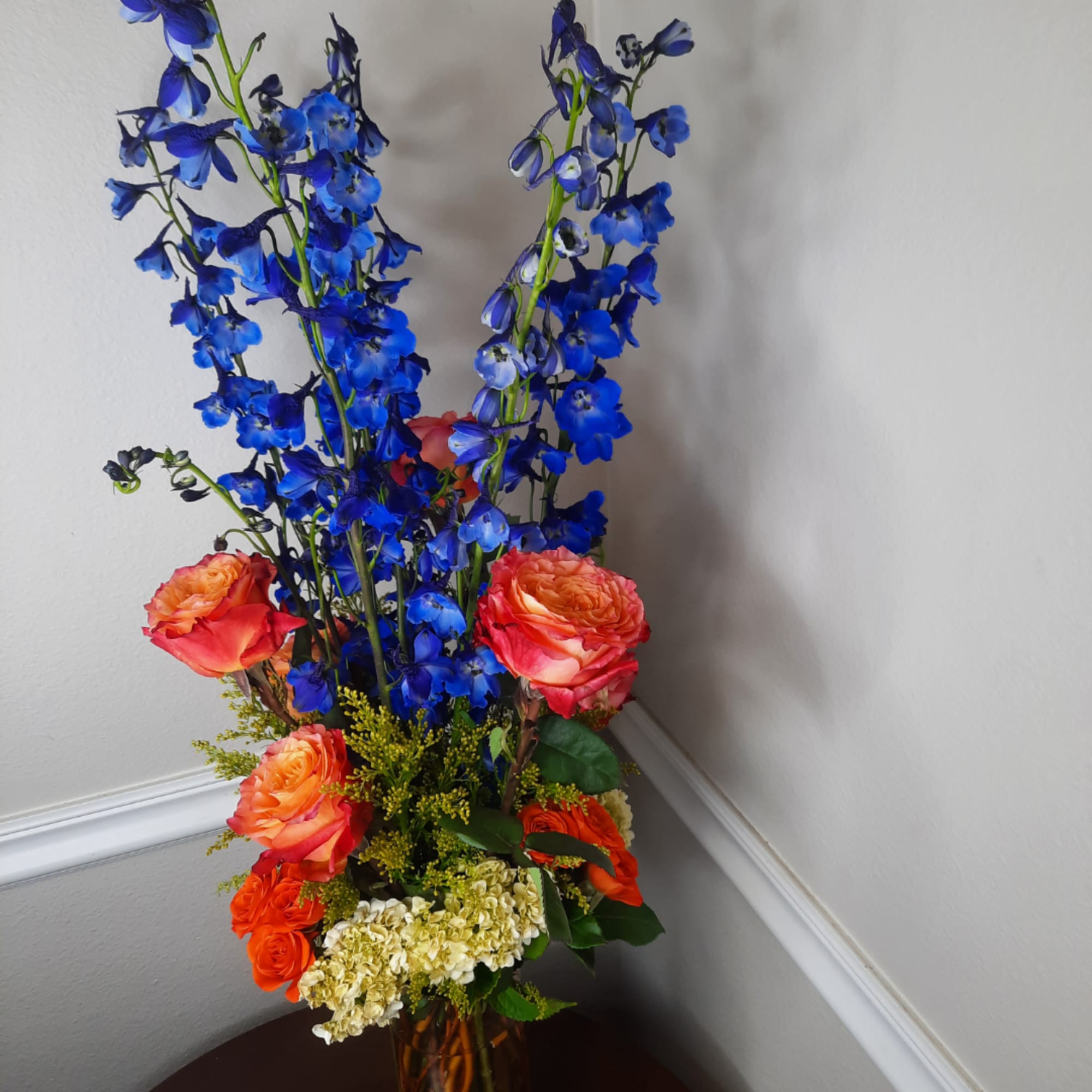 Tall bouquet of blue delphinium and orange roses in a vase