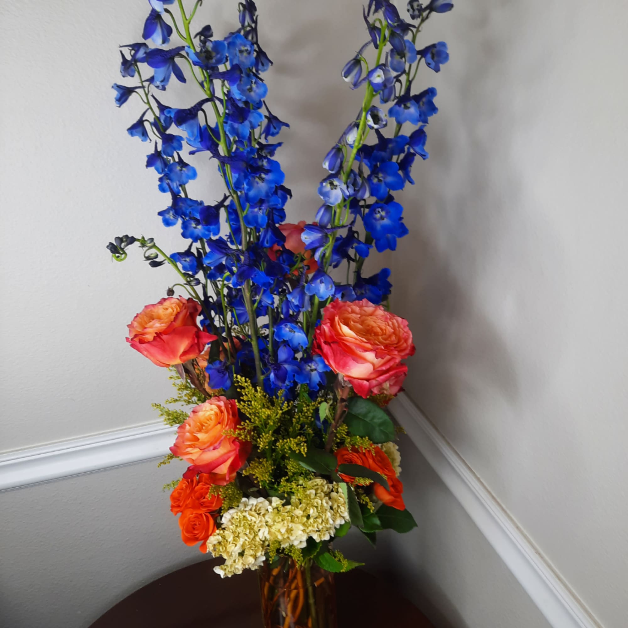 Tall bouquet with blue delphinium and orange roses in a glass vase