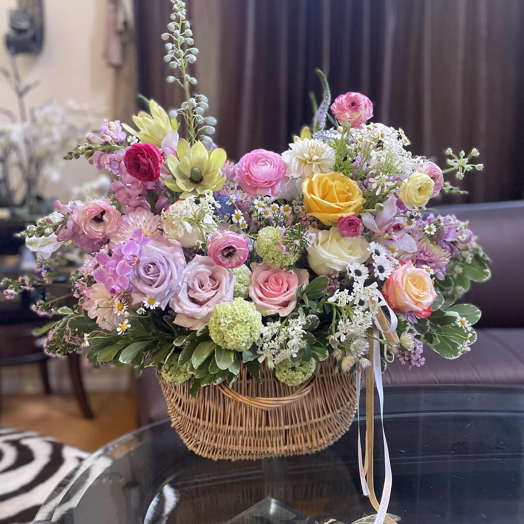 Mixed pastel flower arrangement in a wicker basket with ribbon ties