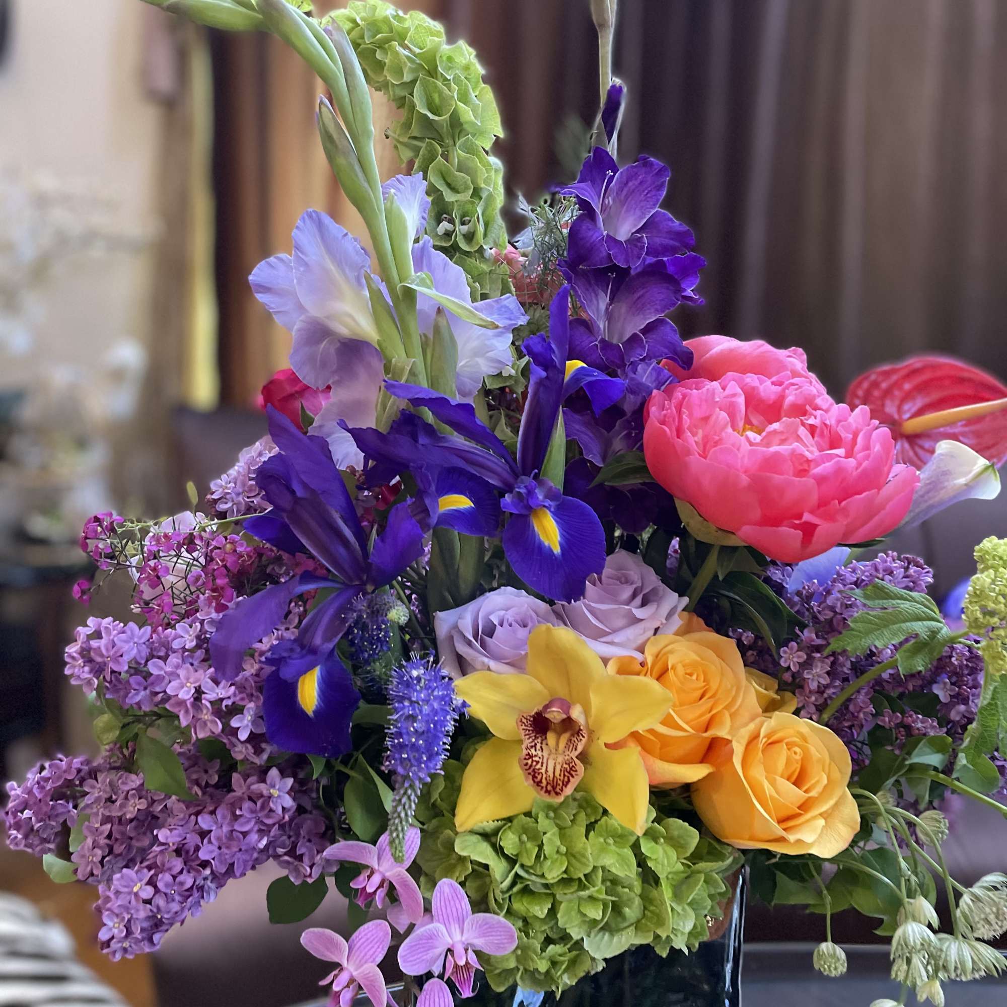Mixed bouquet with purple irises, pink peonies, yellow orchids, and roses in a black vase