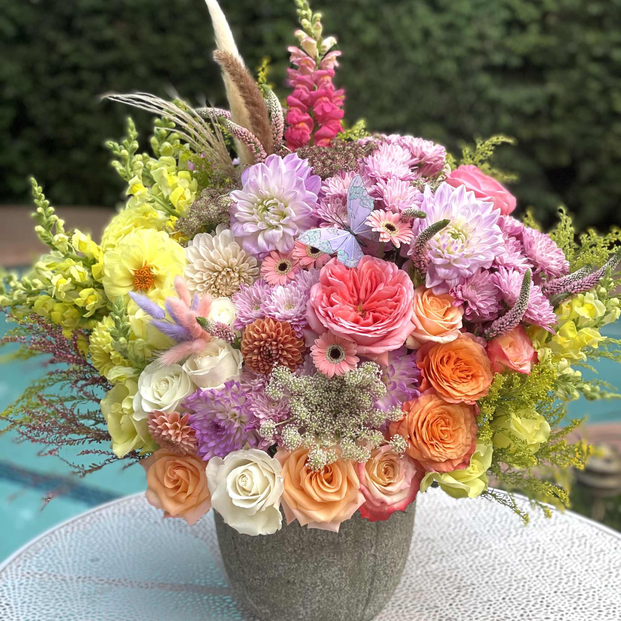 Colorful mixed flower arrangement in a gray vase with a butterfly accent