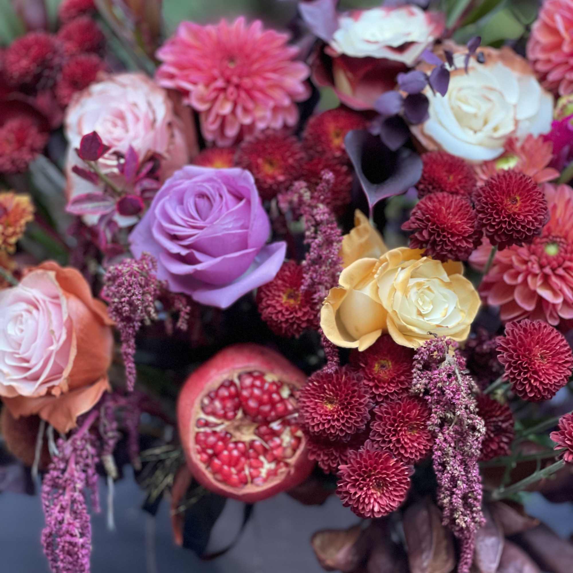 Mixed bouquet of roses, dahlias, and pomegranates in a vase