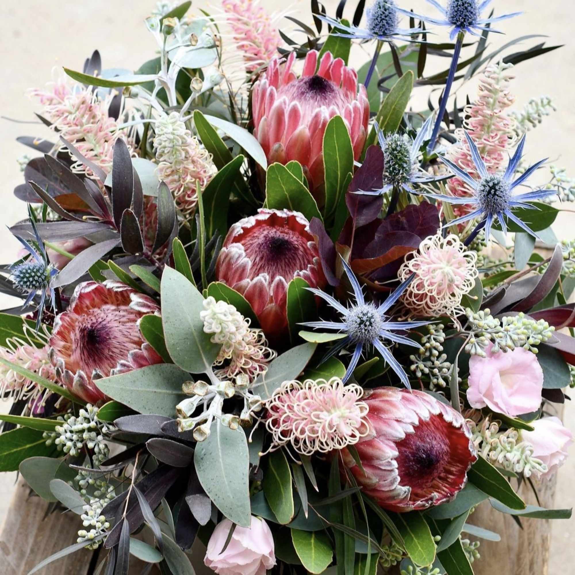 Mixed bouquet with pink protea and blue thistle in a low container