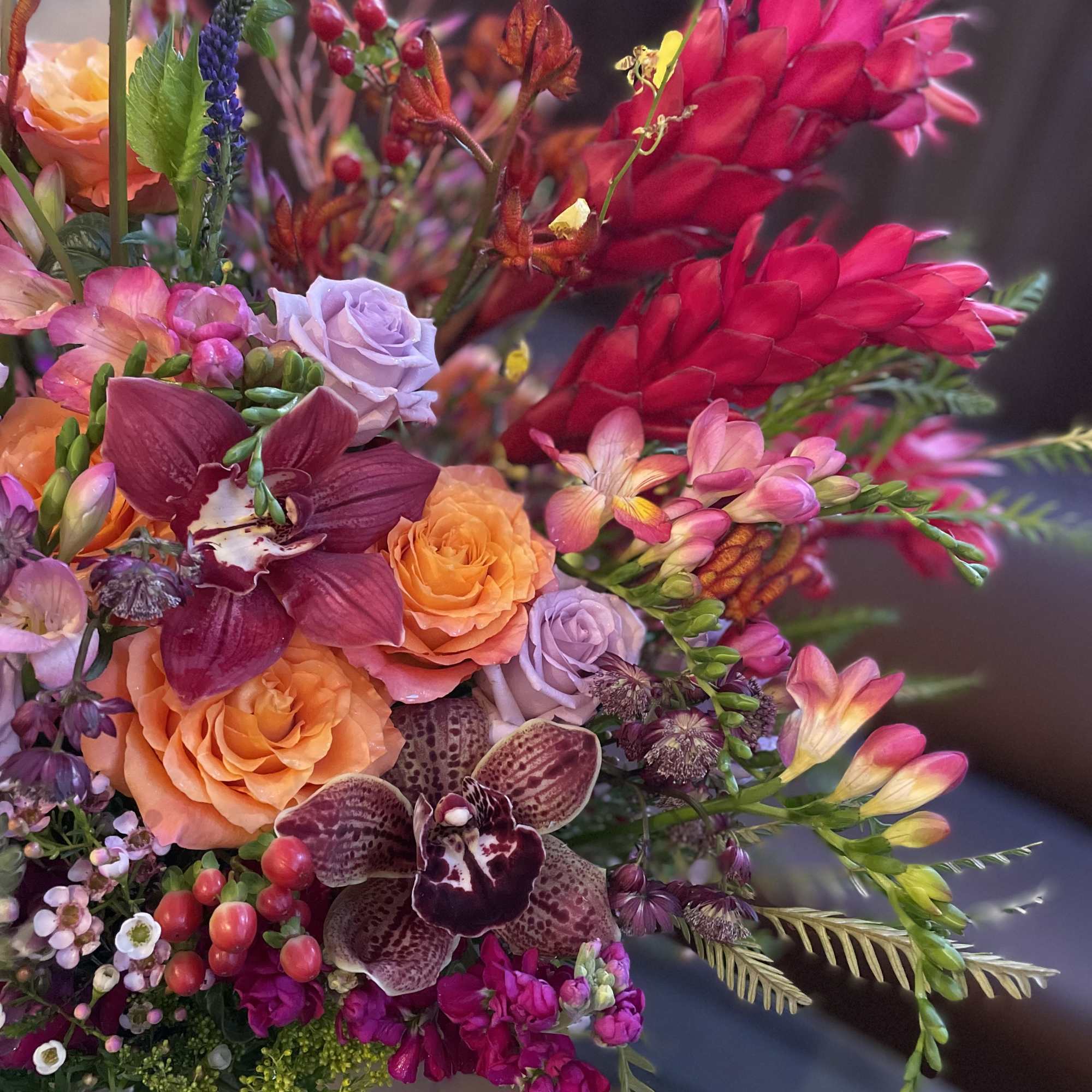 Colorful bouquet with orange roses, orchids, and bright pink flowers