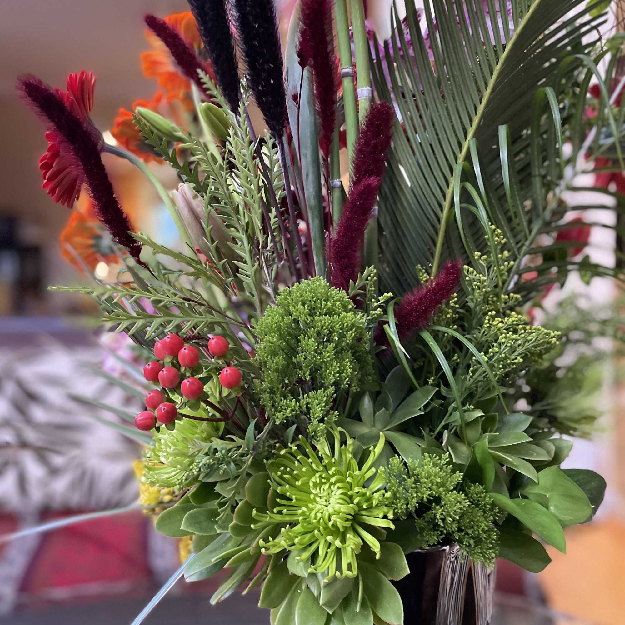Tropical floral arrangement in a glass vase with green succulents and burgundy accents
