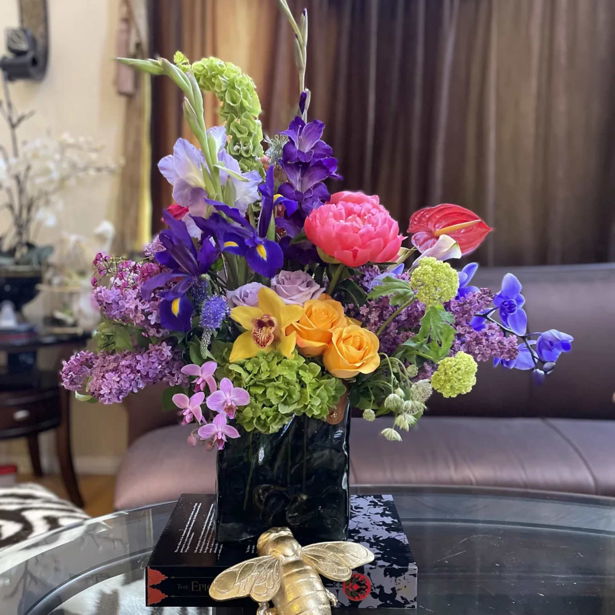 Colorful mixed flower arrangement in a black vase with a gold bee ornament