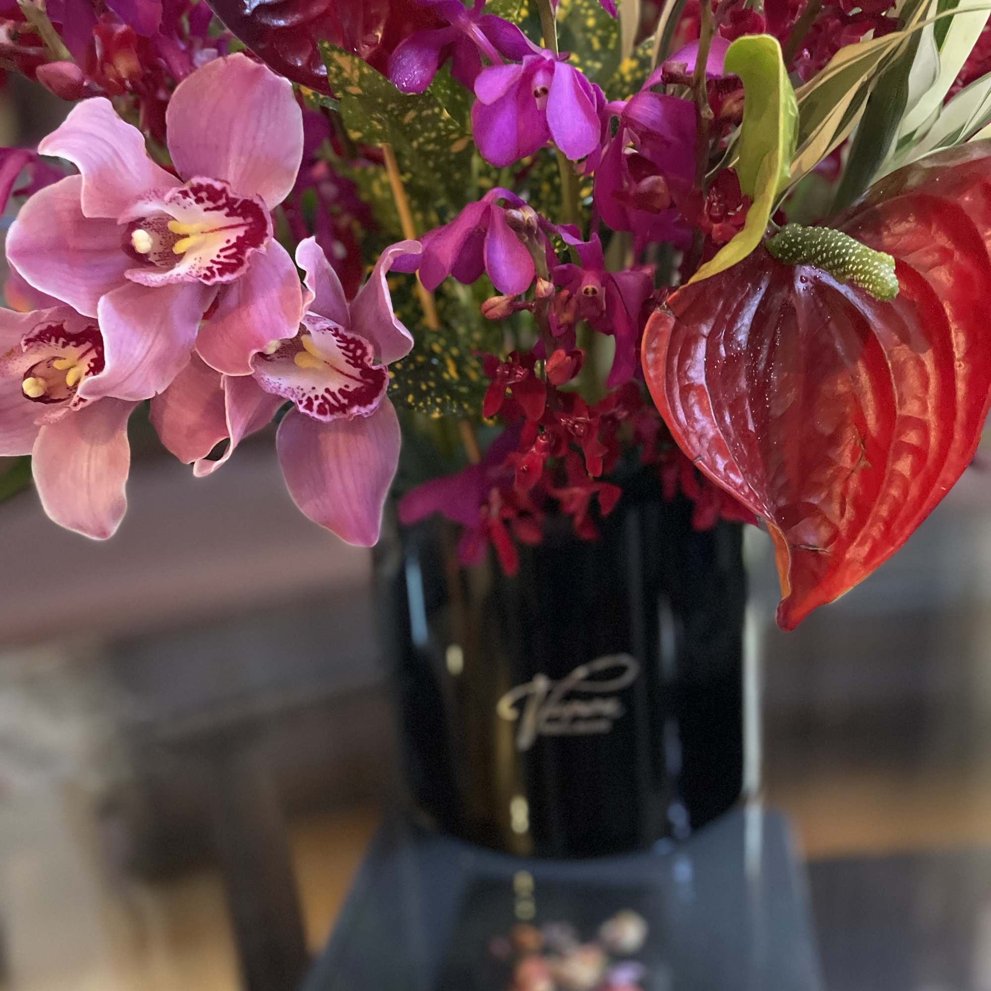 Pink orchids and a red anthurium in a black vase