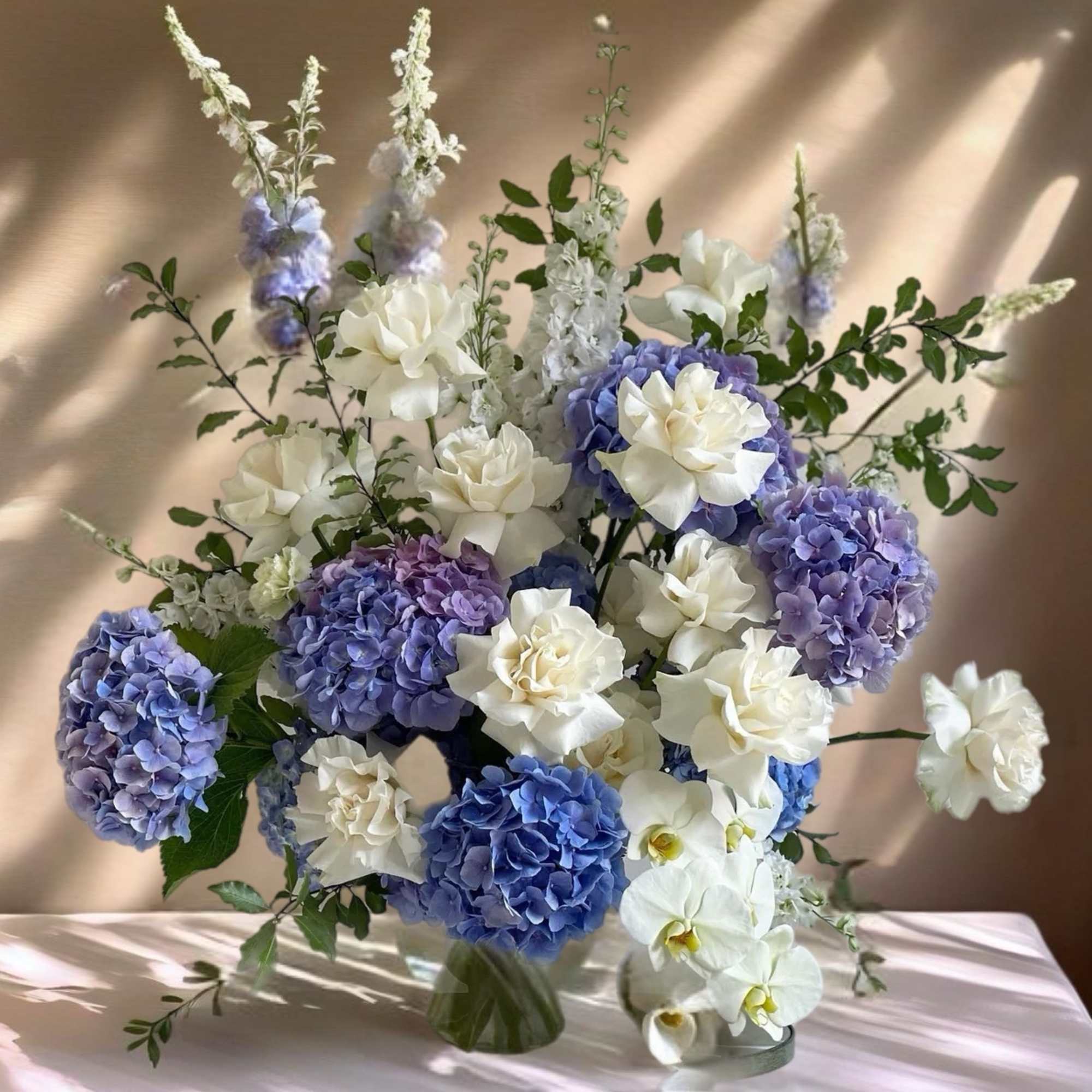 Blue and white floral arrangement with hydrangeas and orchids in a glass vase