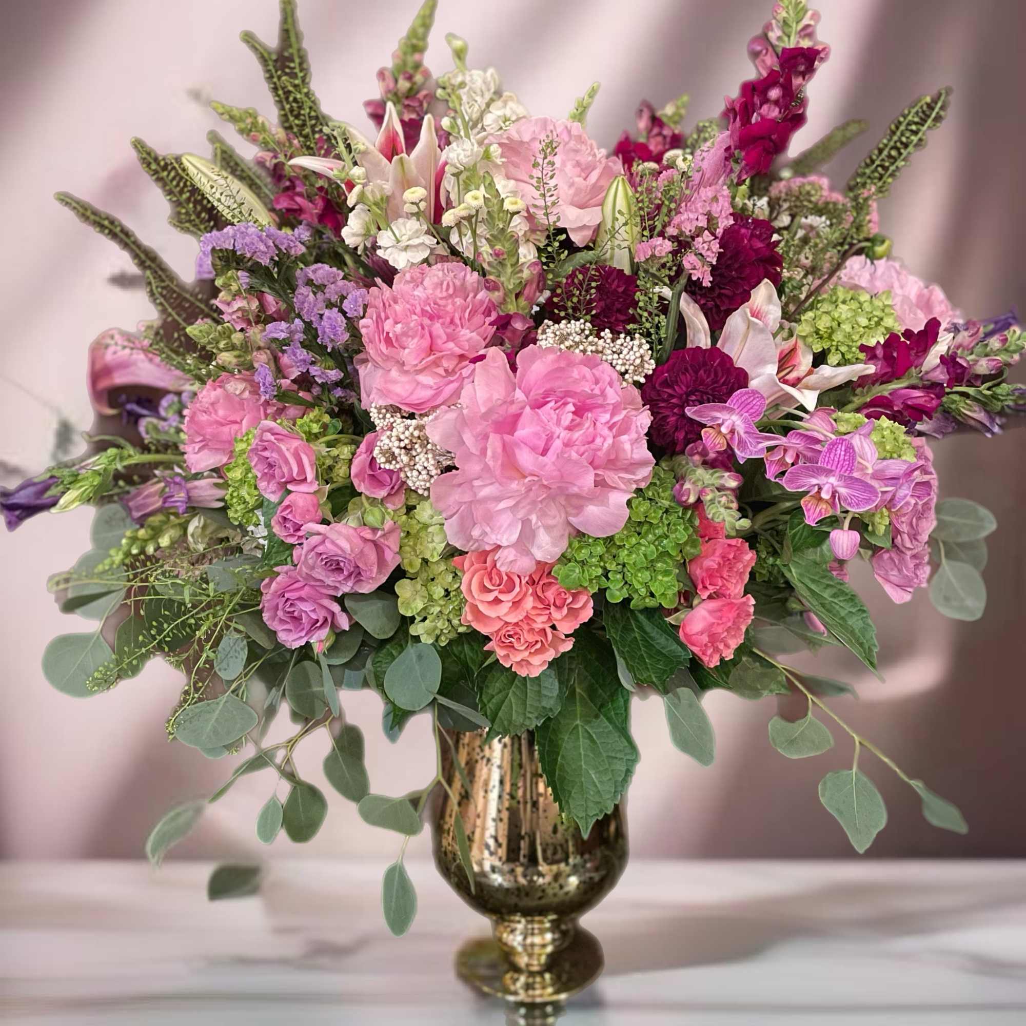 Large pink and purple floral arrangement in a gold vase