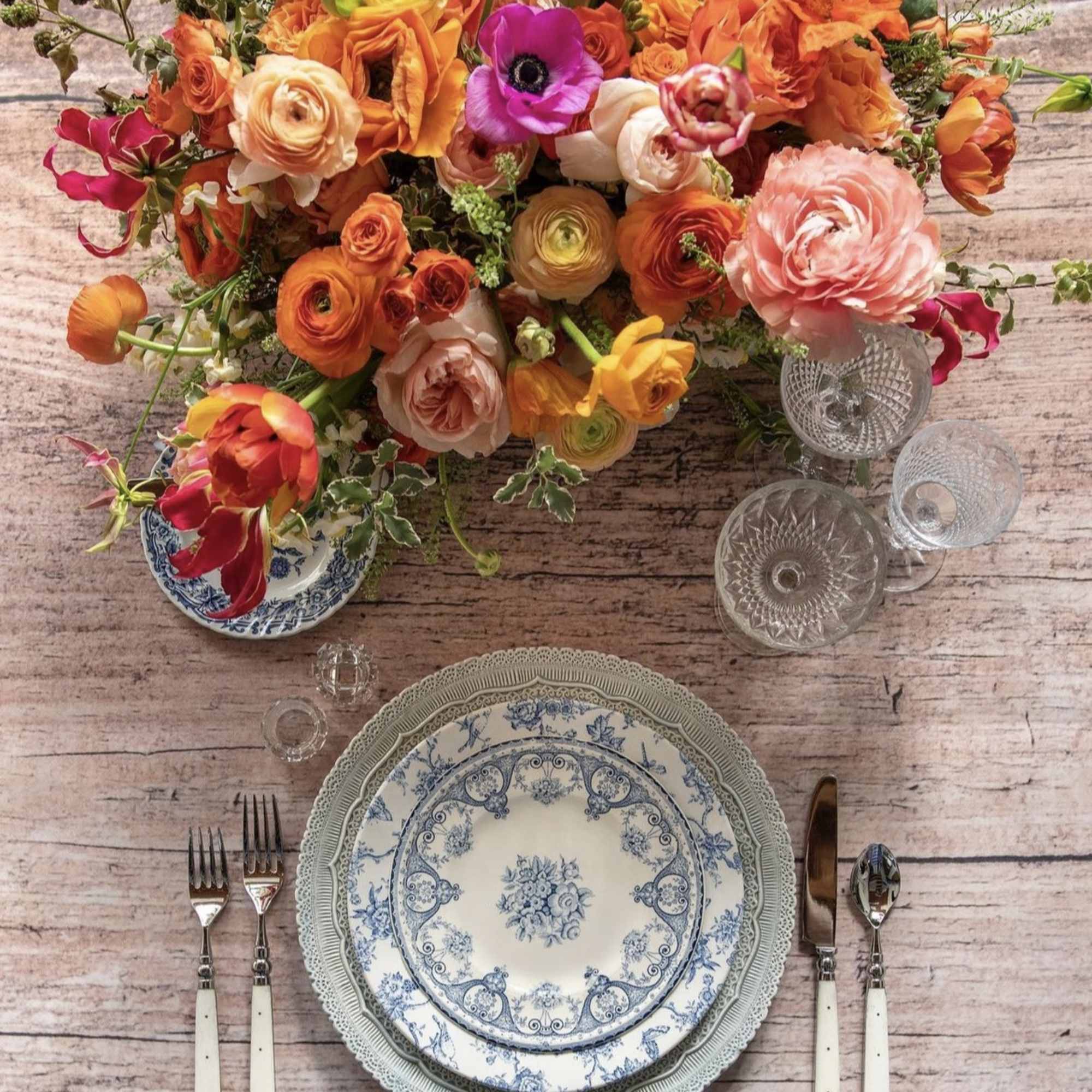 Bright mixed flower arrangement above a set table with patterned plates