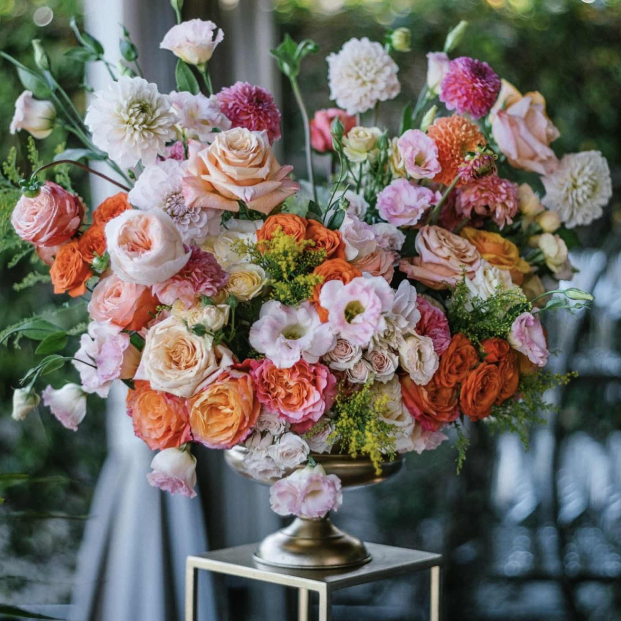 Large mixed bouquet of peach, pink, and white flowers in a gold pedestal vase