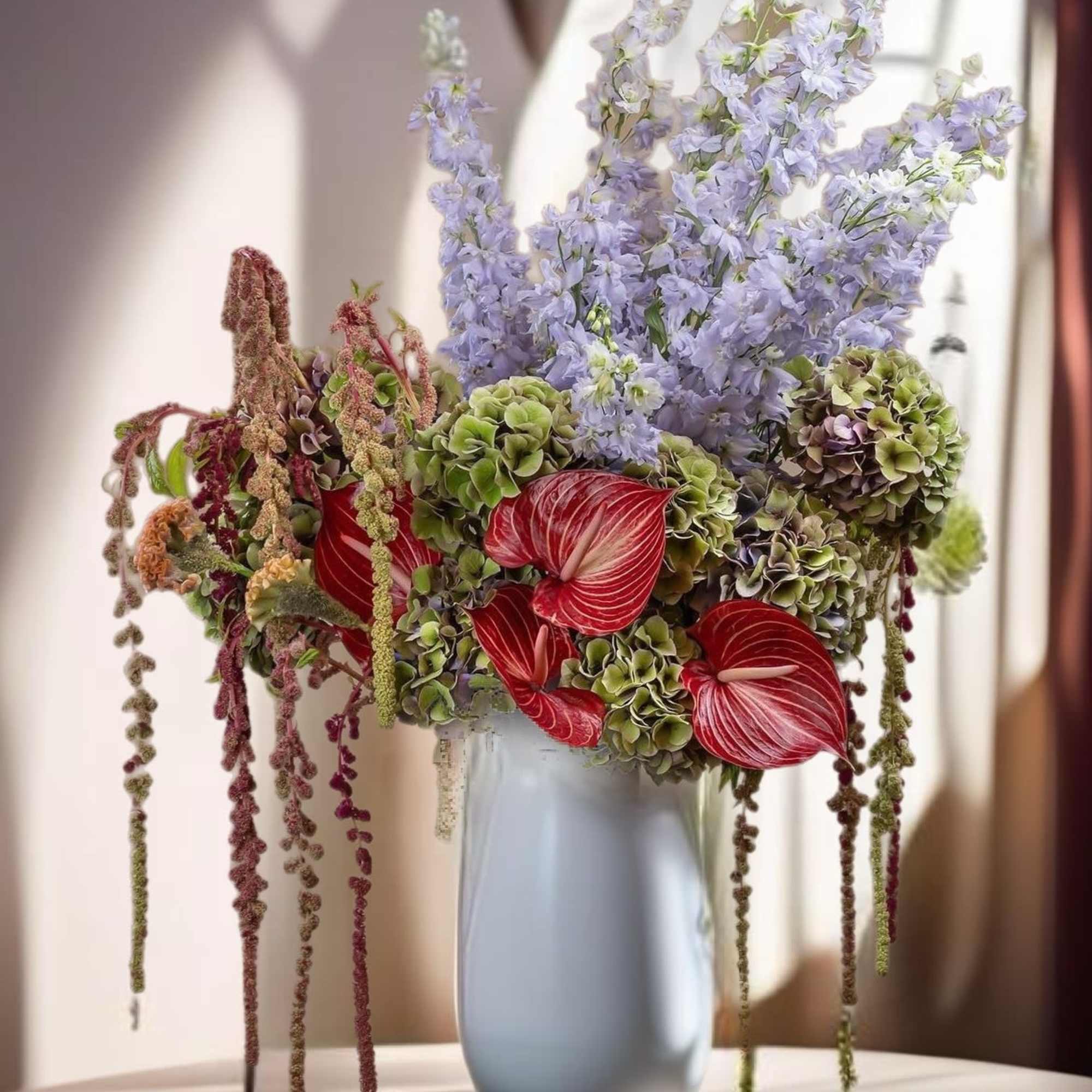 Tall bouquet of lavender flowers, green hydrangeas, and red anthuriums in a vase