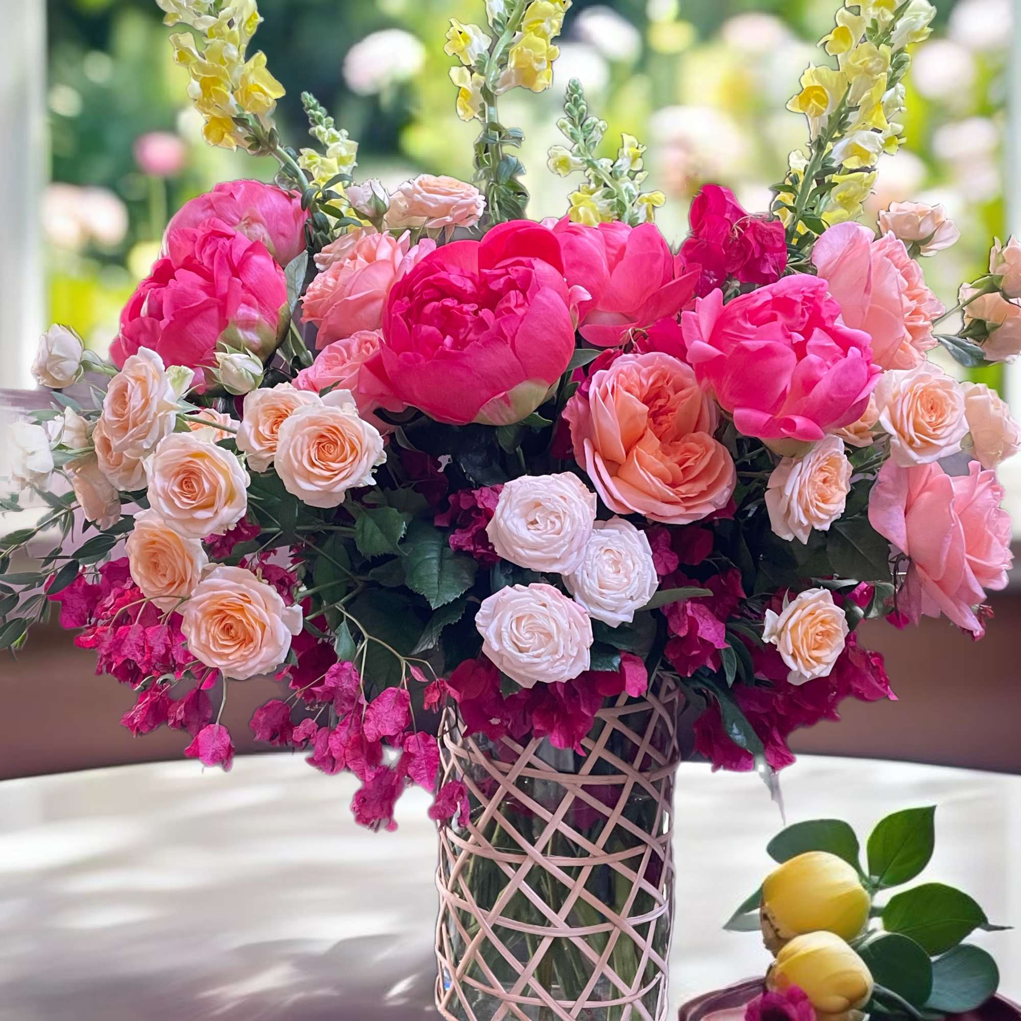 Pink and peach floral arrangement in a glass vase with yellow snapdragons