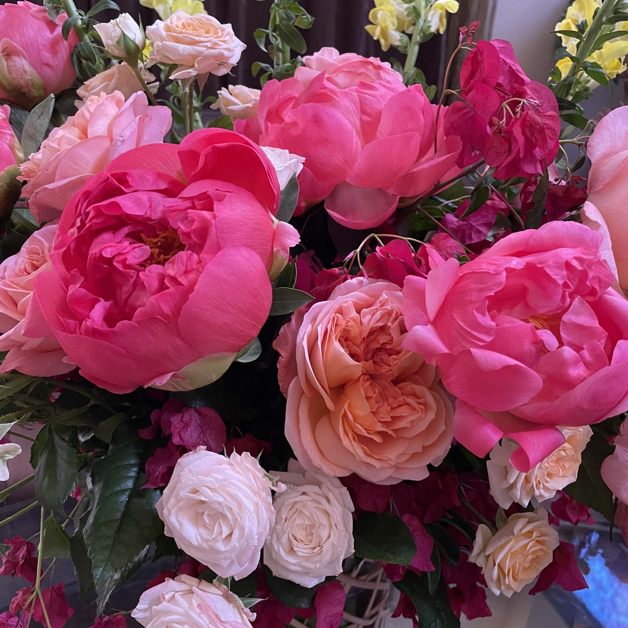 Pink and peach roses arranged with yellow snapdragons in a vase