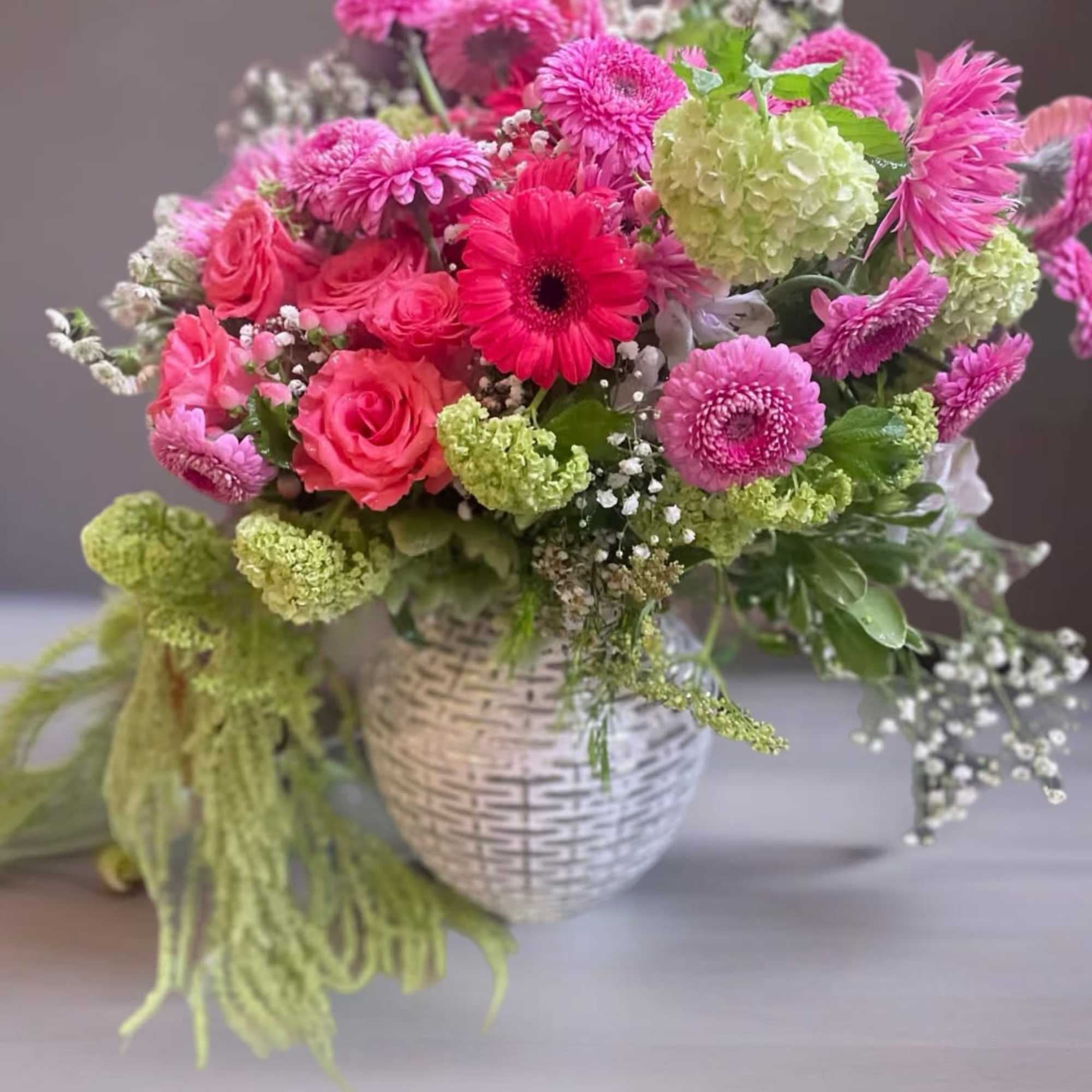 Pink and green mixed flower arrangement in a white woven vase