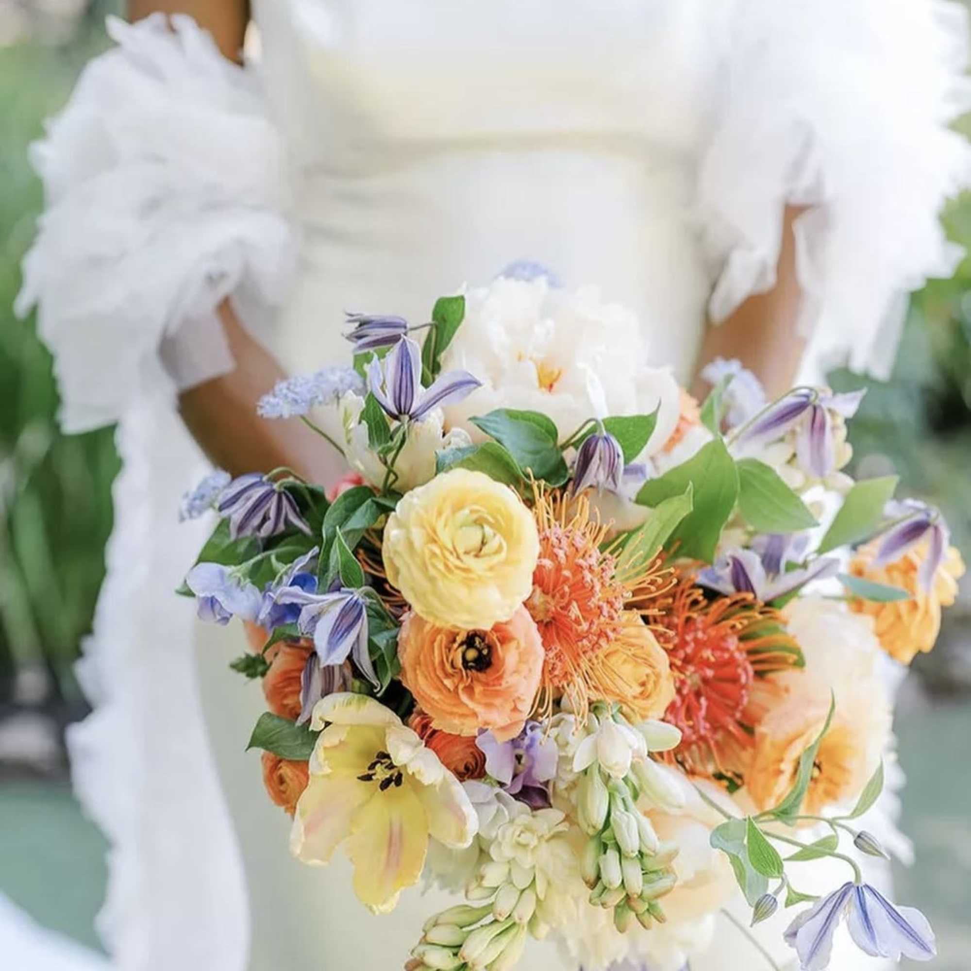 Bride holding a colorful bouquet with orange, yellow, white, and lavender flowers