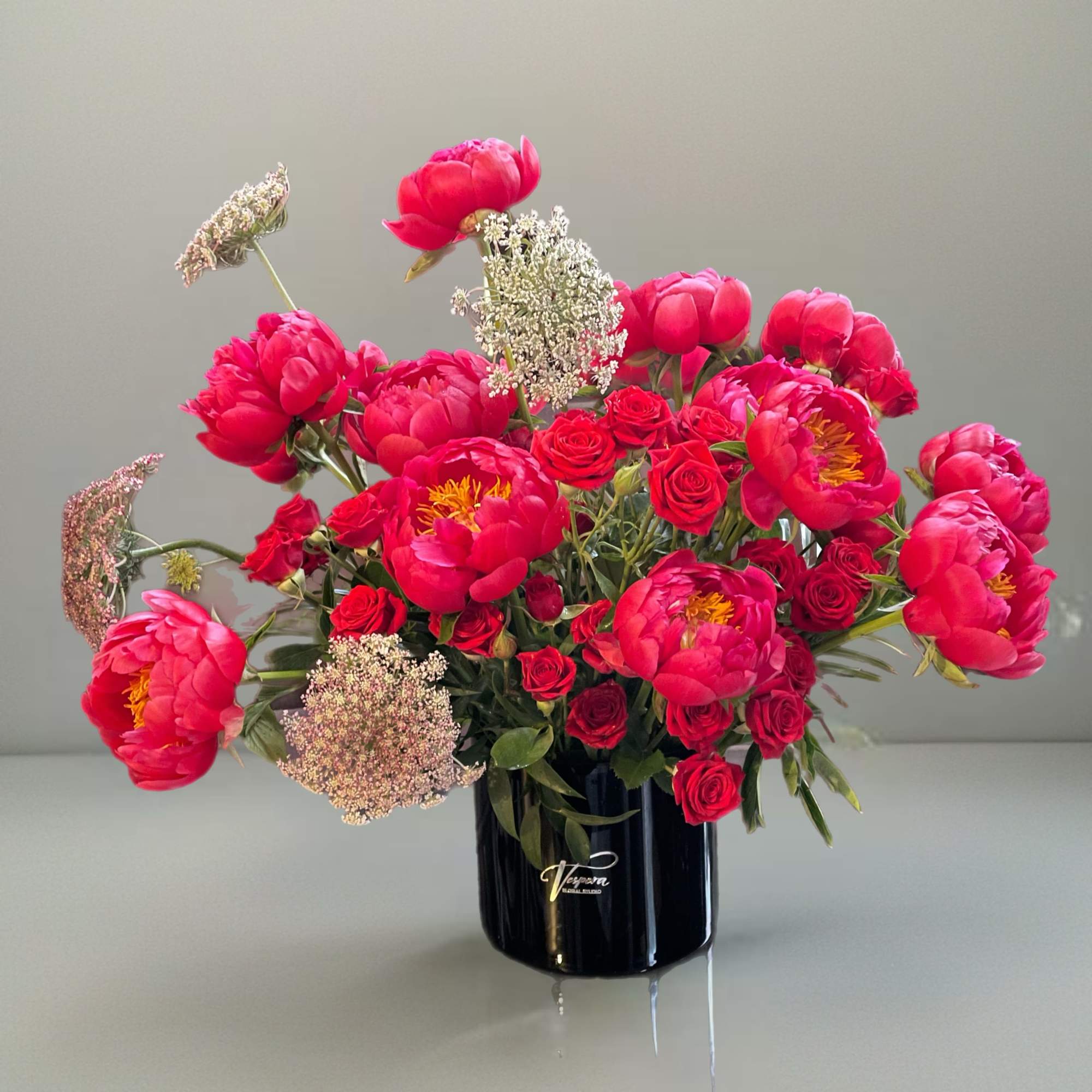 Pink peonies and red roses arranged in a black vase