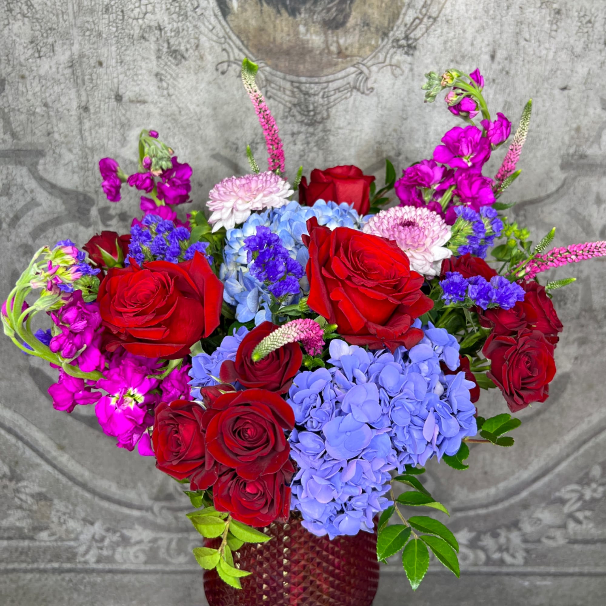 Red roses and blue hydrangeas in a textured vase with pink accent flowers