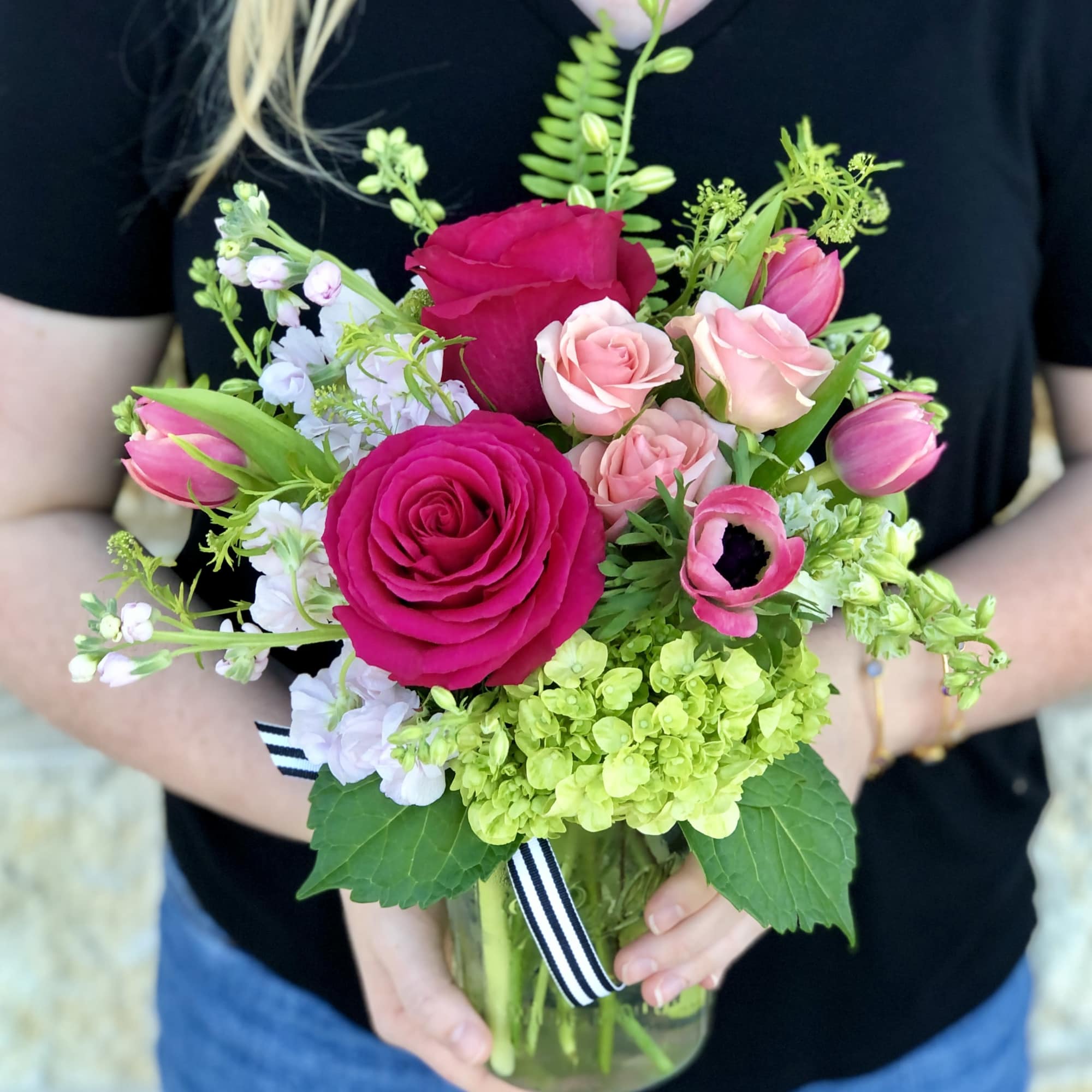 Handheld bouquet of pink roses, tulips, and white blooms in a glass vase